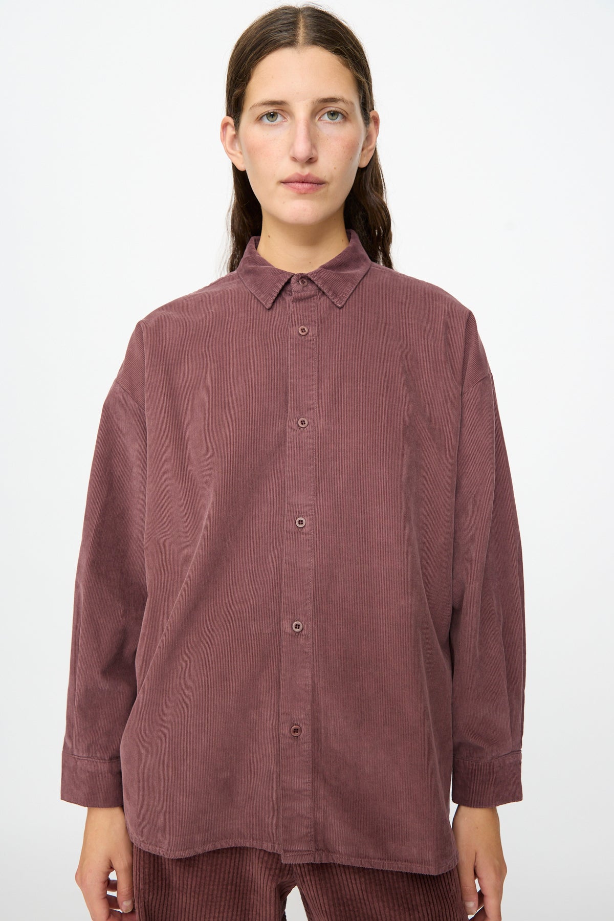 A person wearing the Labo.Art Quadra Shirt in Sasso—a relaxed fit mauve cotton needlecord button down shirt—with matching pants, standing against a plain white background.