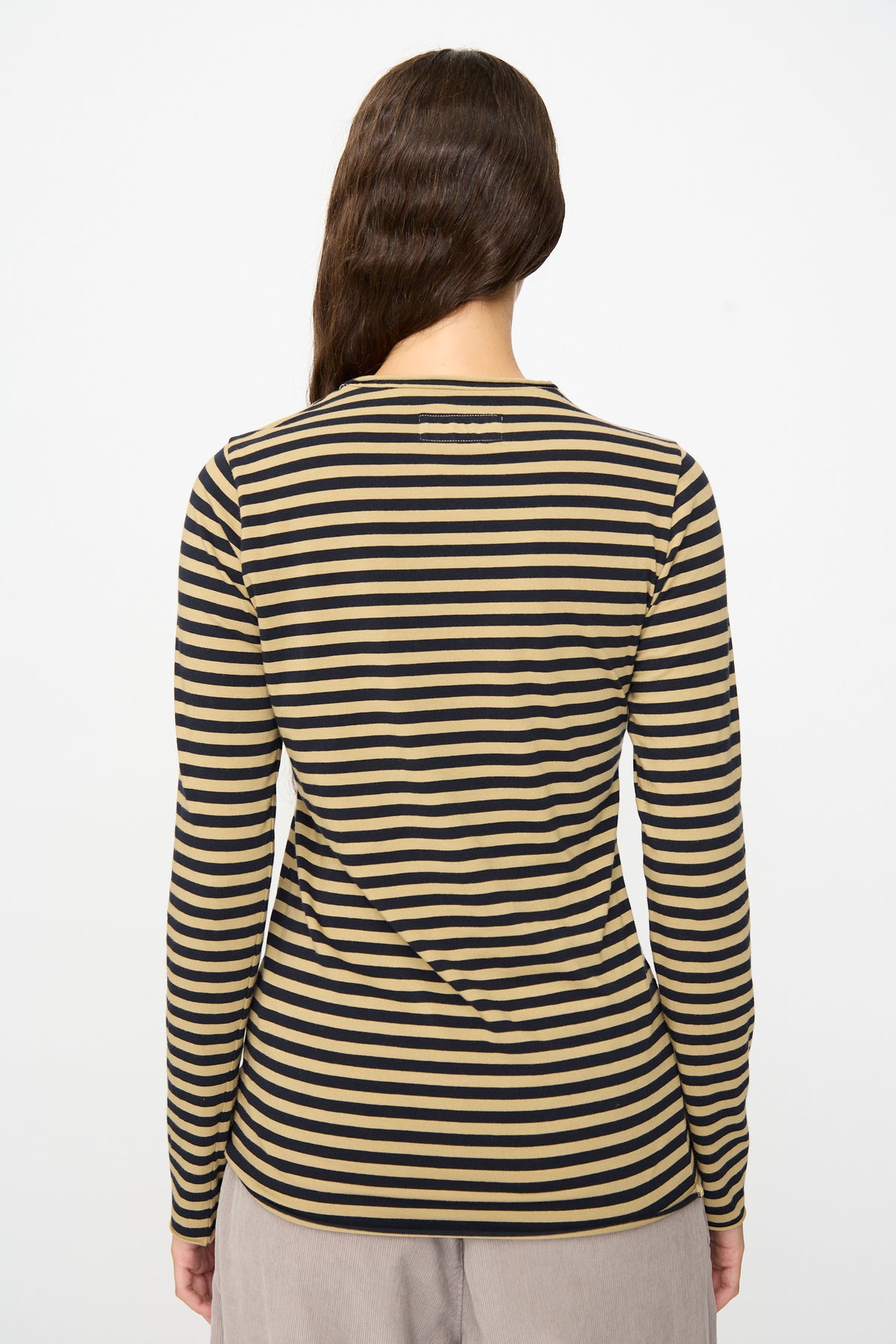 A person stands with their back to the camera, wearing the Labo.Art Striped Jersey Basic Longsleeve in Fennec and light-colored pants, set against a plain white background.