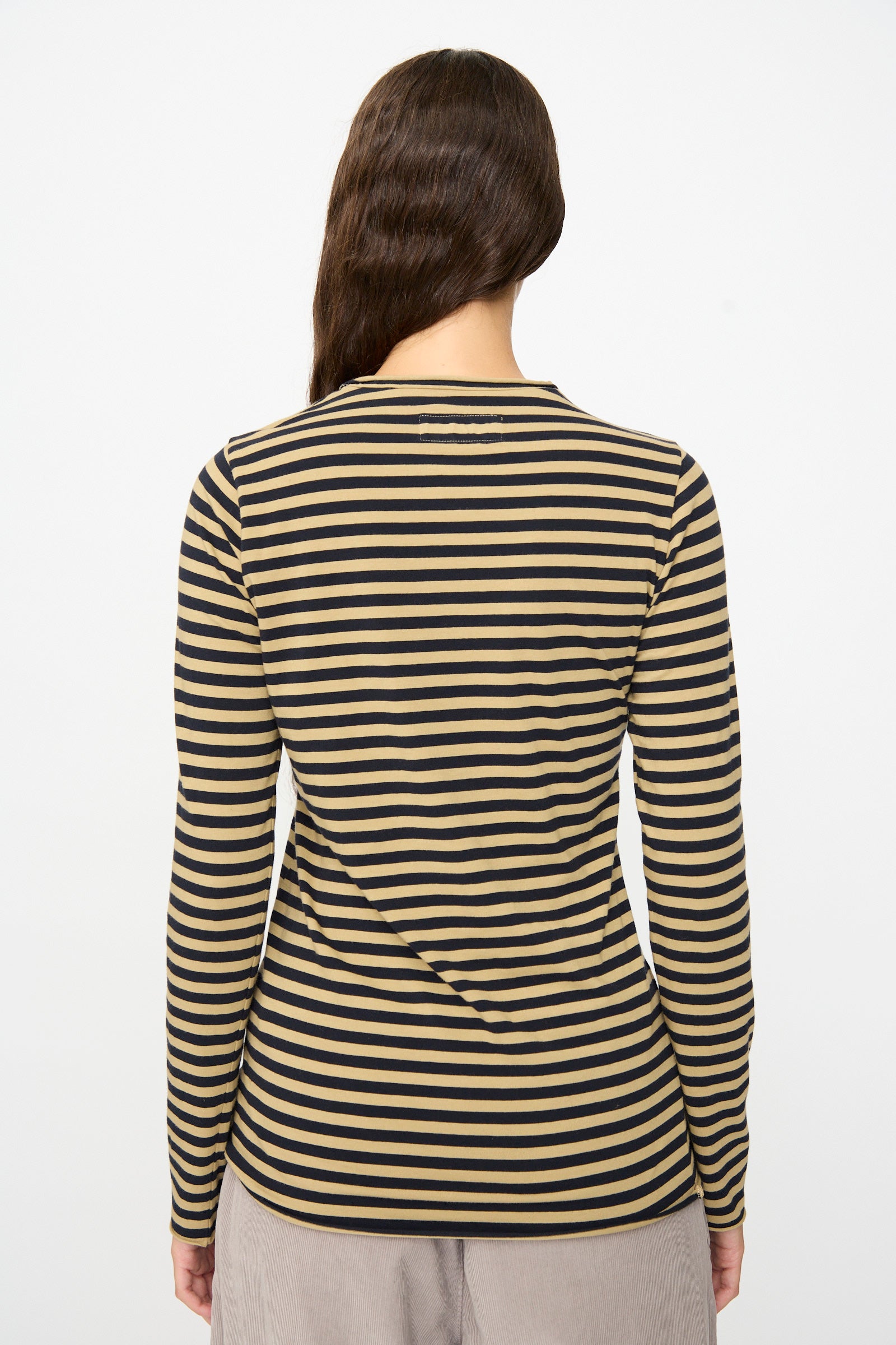 A person stands with their back to the camera, wearing the Labo.Art Striped Jersey Basic Longsleeve in Fennec and light-colored pants, set against a plain white background.