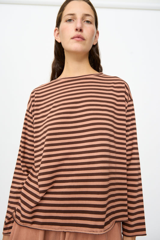 A person wearing the Labo.Art Striped Jersey Lola Sweater in Canyon, a loose-fitting brown and black striped long sleeve cotton top, stands against a plain white background.