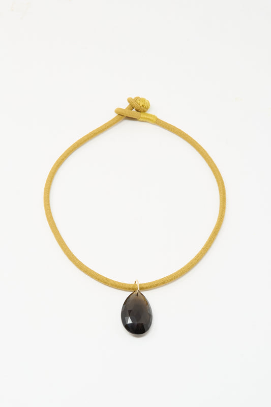 The Drop Cord in Tan and Smoky Quartz by Laoli features a handmade 14k yellow gold cord necklace with a knotted clasp and a large, teardrop-shaped smoky quartz pendant at the center.