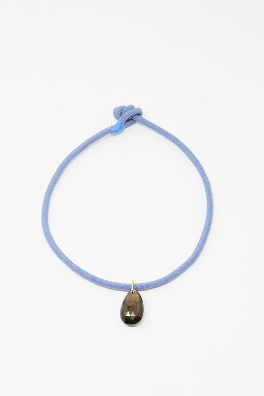 The Petite Drop Cord in Blue and Smoky Quartz by Laoli is a handmade Parisian necklace with a light blue cord, knotted design, and a single teardrop-shaped smoky quartz pendant, shown on a plain white background.