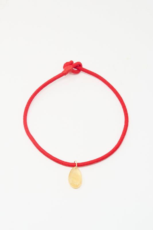 The Petite Drop Cord in Red and Citrine by Laoli is a simple red bracelet with a single oval citrine-like stone, shown on a white background.