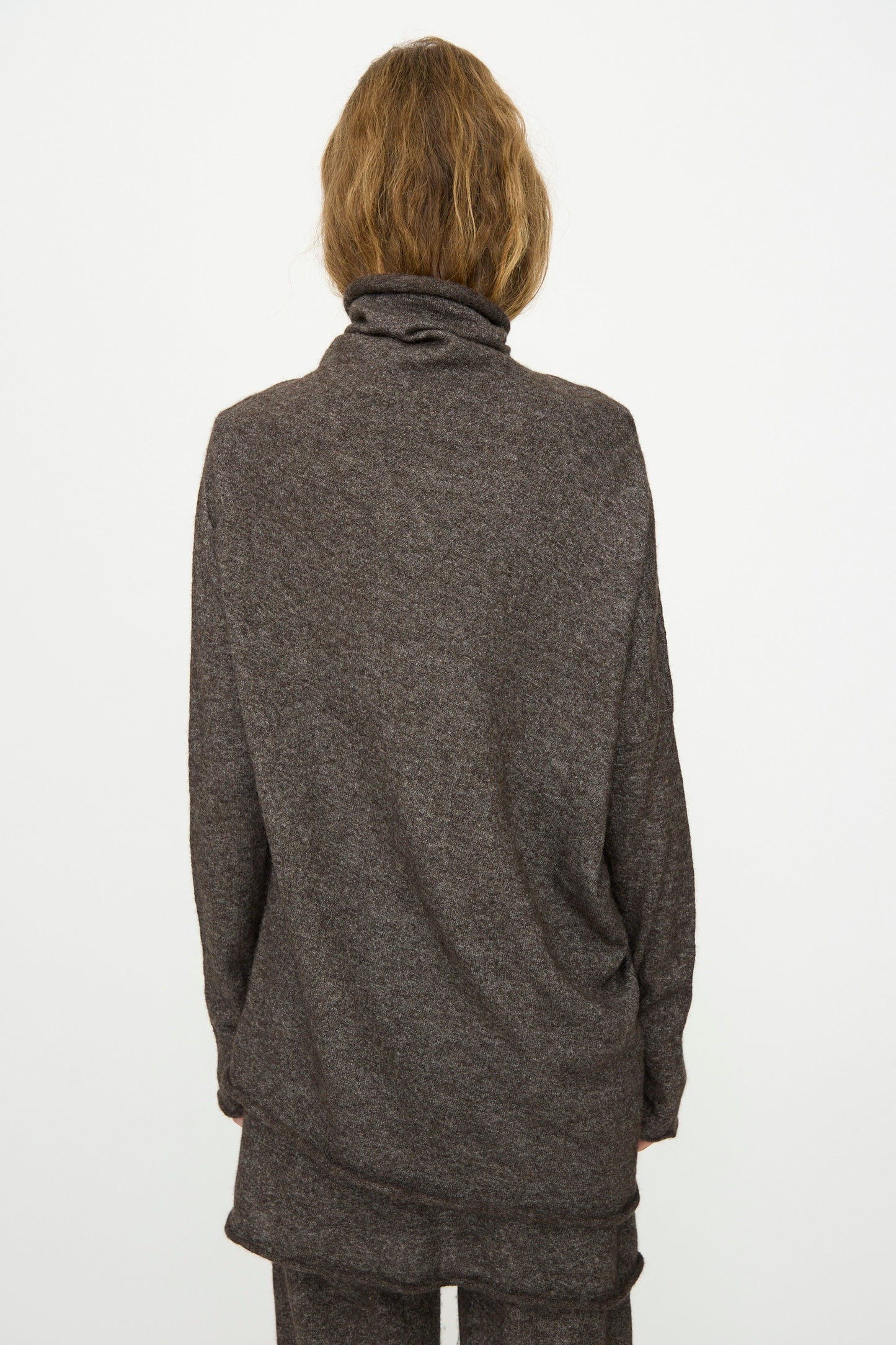Person with medium-length light brown hair wears the Lauren Manoogian Askew Funnel Sweater in Blackened, relaxed fit, photographed from the back against a plain white background.