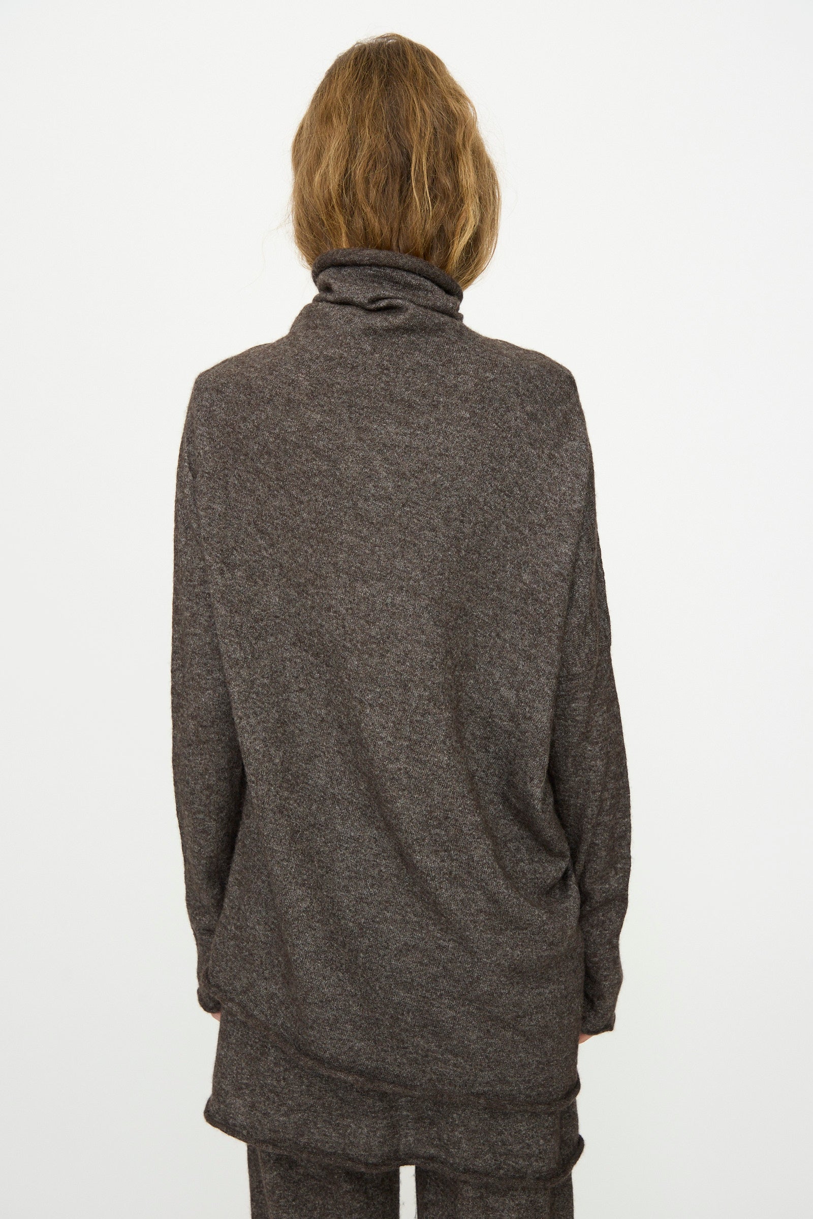 Person with medium-length light brown hair wears the Lauren Manoogian Askew Funnel Sweater in Blackened, relaxed fit, photographed from the back against a plain white background.
