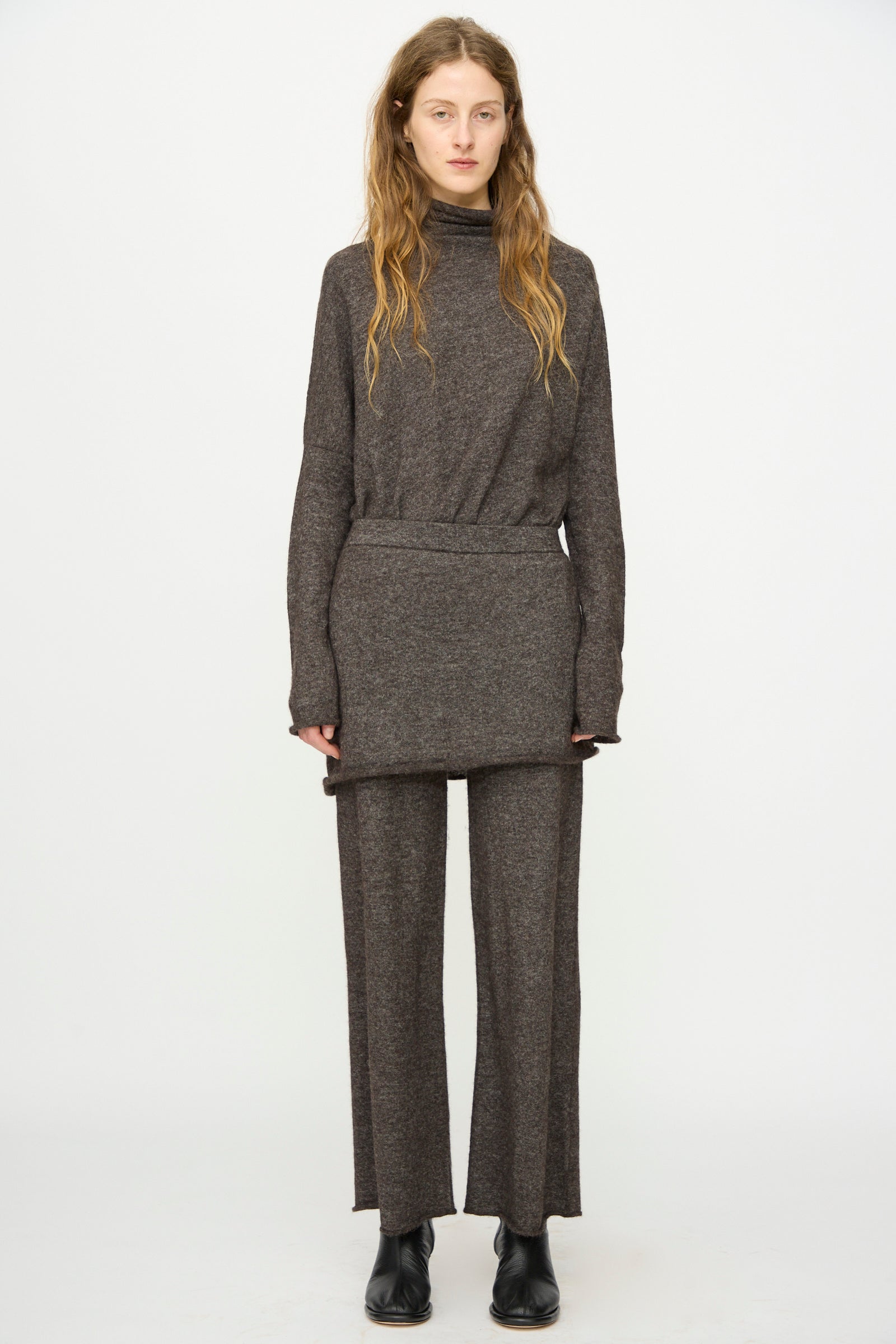 A person stands facing forward wearing a brown long-sleeve turtleneck top, Lauren Manoogian Askew Layer Pants in Blackened, and black shoes against a plain white background.