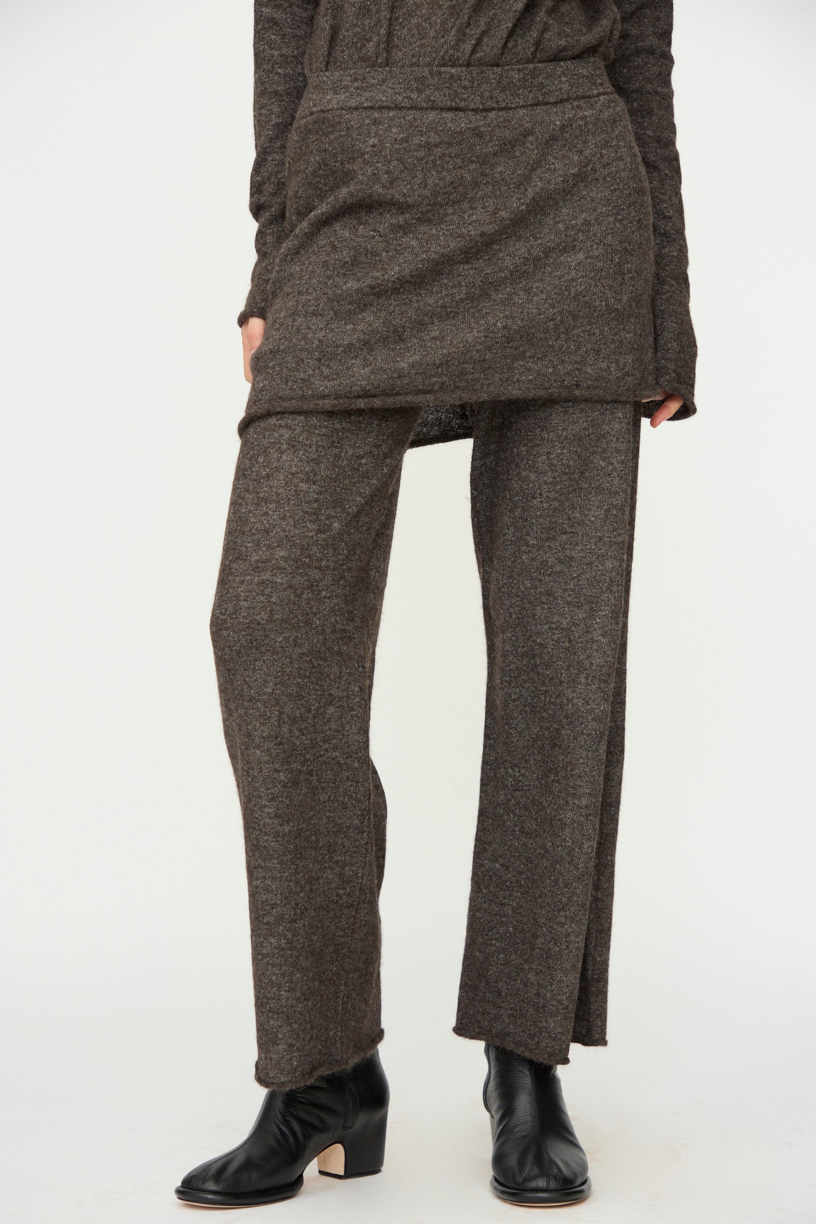 A person wears a brown long-sleeve top and skirt layered over Lauren Manoogian Askew Layer Pants in Blackened with black ankle boots, set against a plain white background.