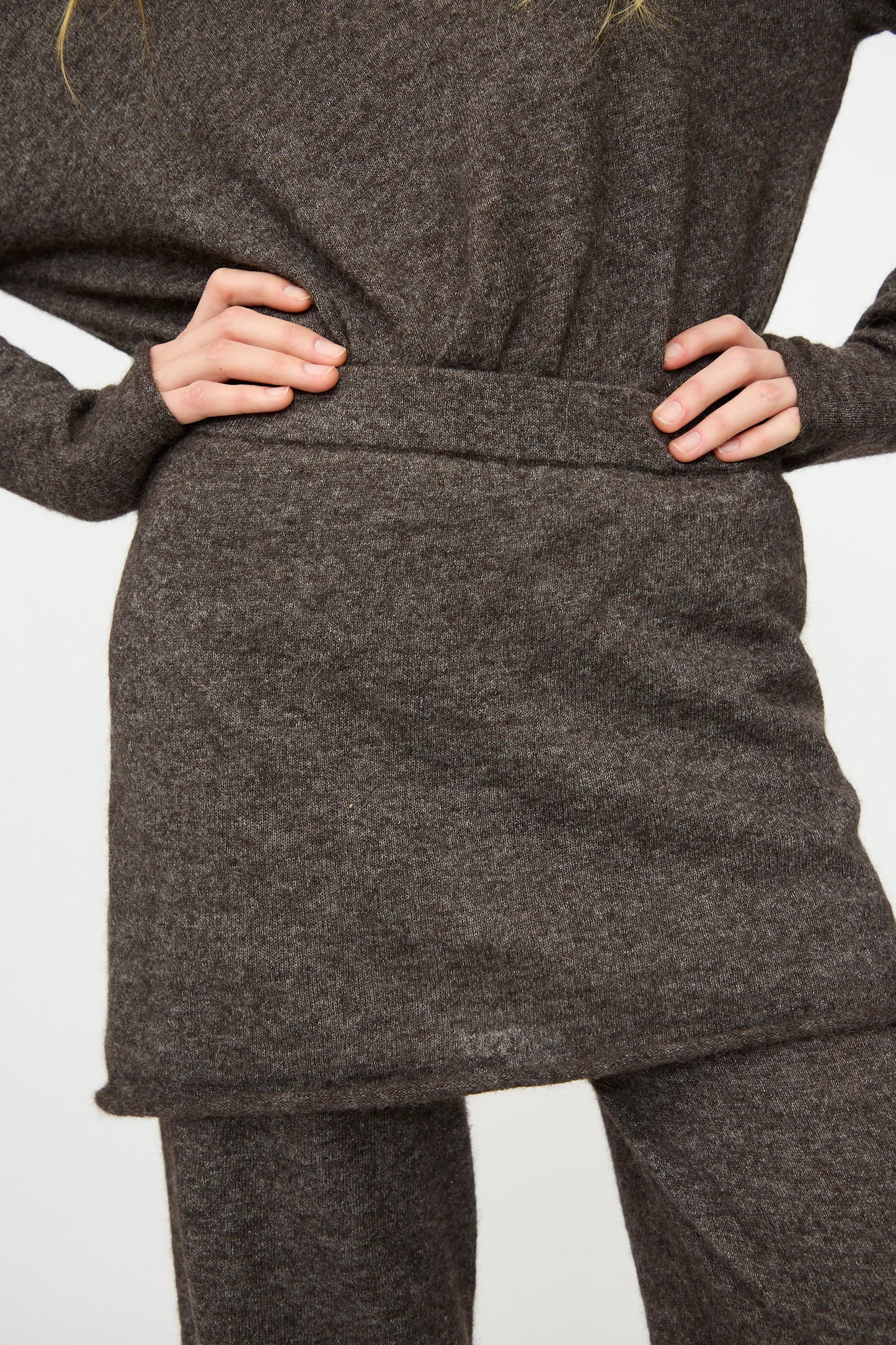 Person wearing a brown knit sweater, matching skirt, and Lauren Manoogian Askew Layer Pants in Blackened; hands on hips, midsection view against a plain background.