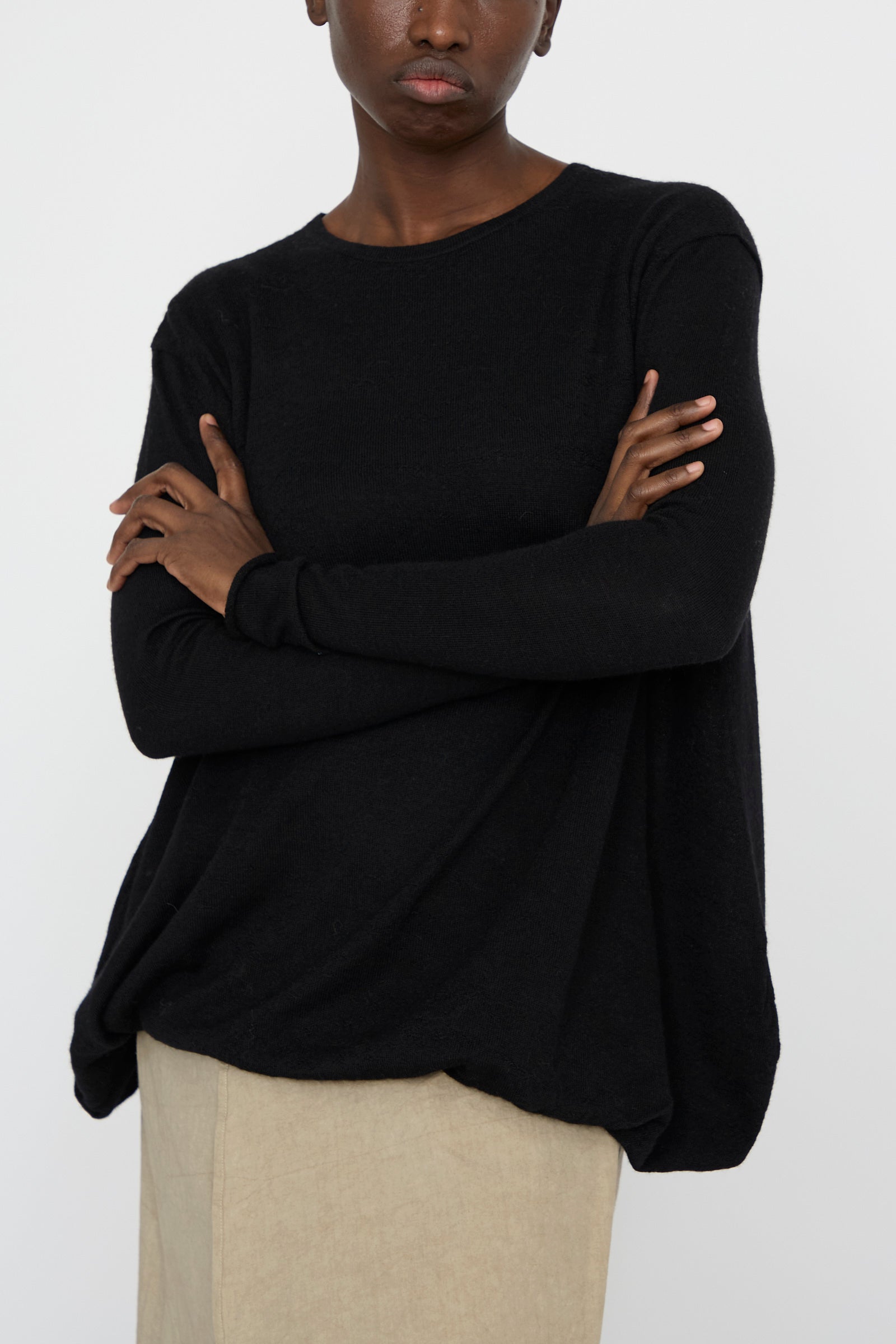 A person wearing a black Lauren Manoogian Balloon Pullover with an oversized fit and beige pants stands with arms crossed against a white background.