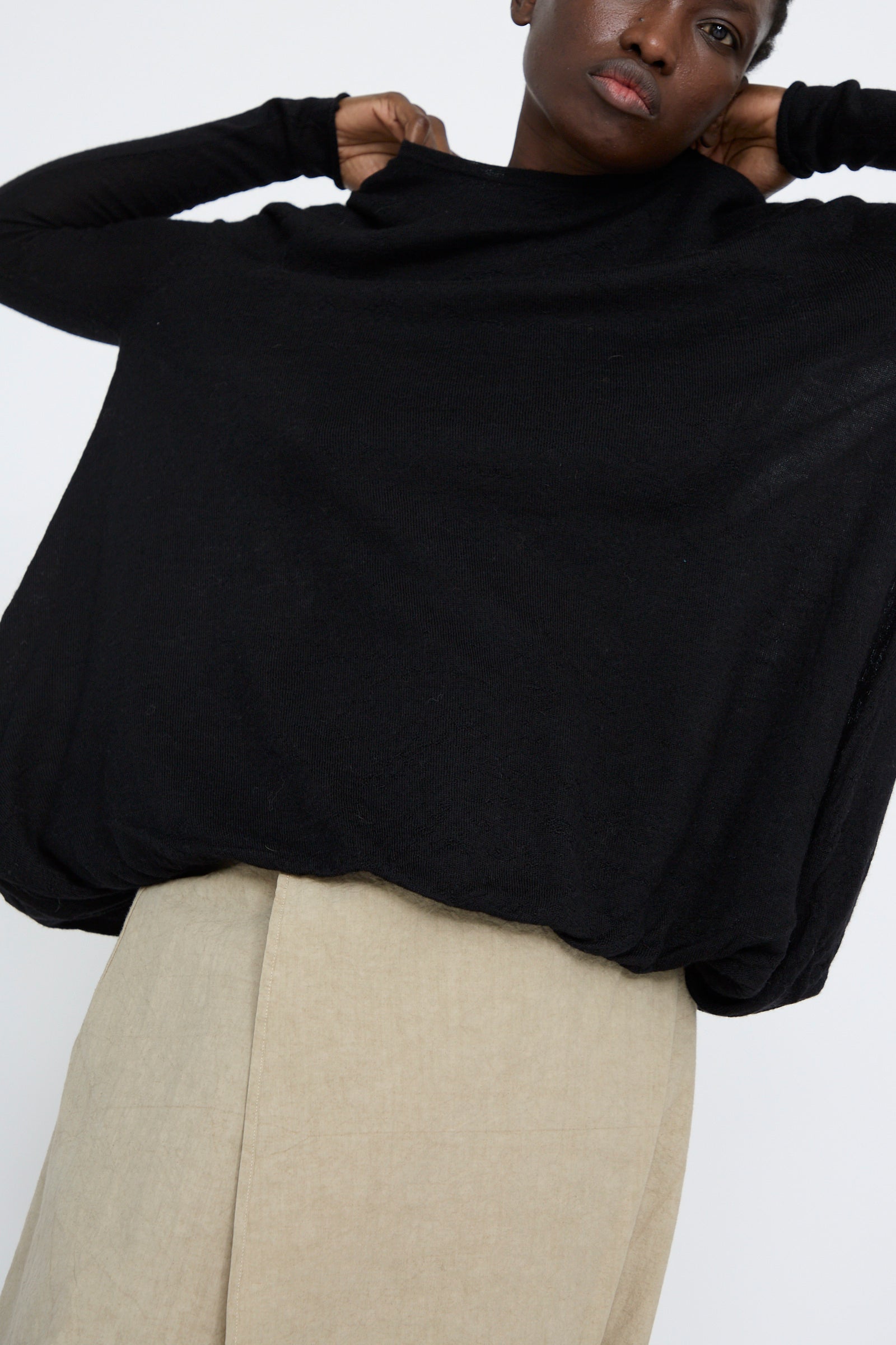 A person wearing a black oversized Balloon Pullover by Lauren Manoogian, made in Peru, paired with beige pants, raises their arms.