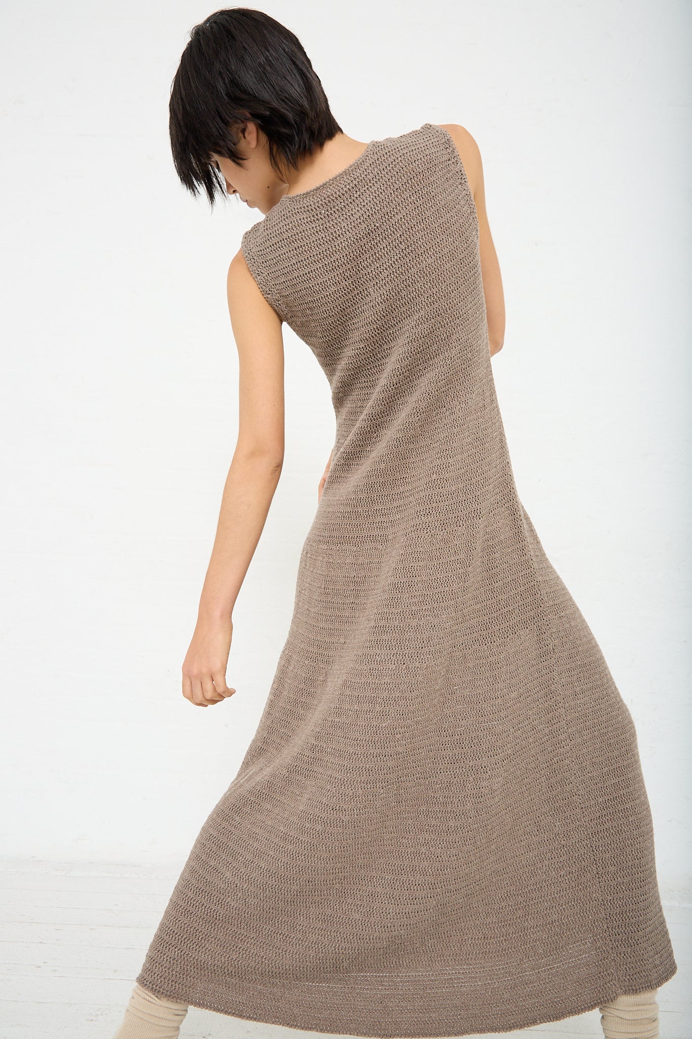 A woman wearing the Lauren Manoogian Basket Dress in Wood (Brown), a sleeveless knitted dress made of pima cotton. Back view.