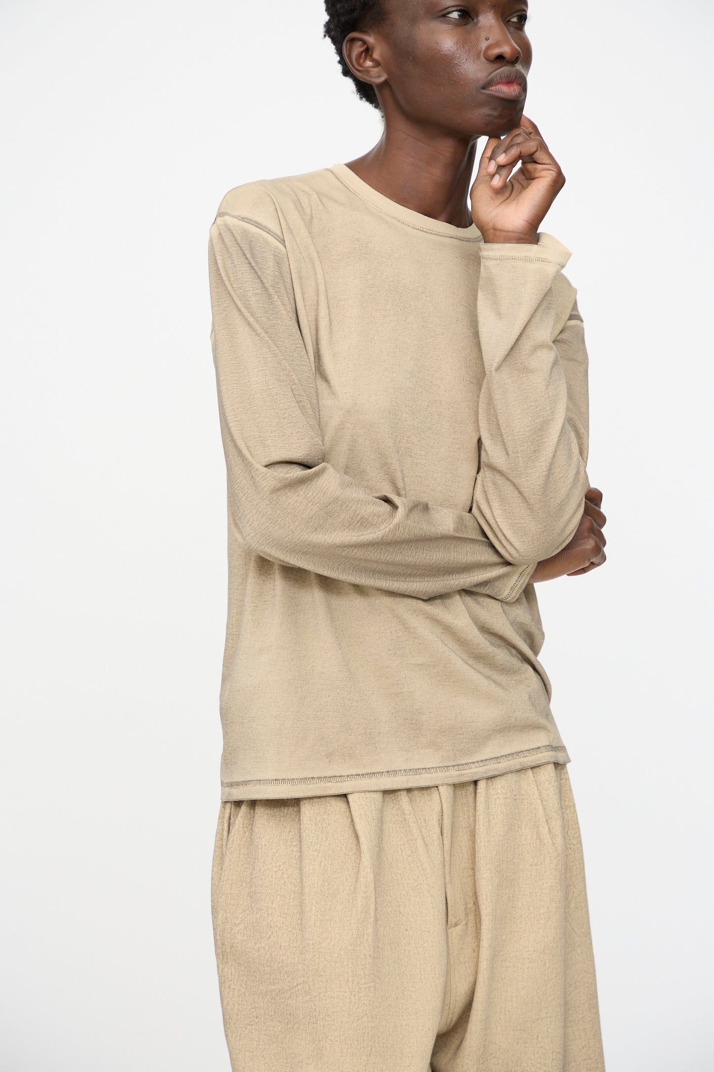 Person wearing the Lauren Manoogian Bias Long Sleeve Tee in Painted Antique, paired with matching loose pants, standing with one hand on their chin against a plain white background.