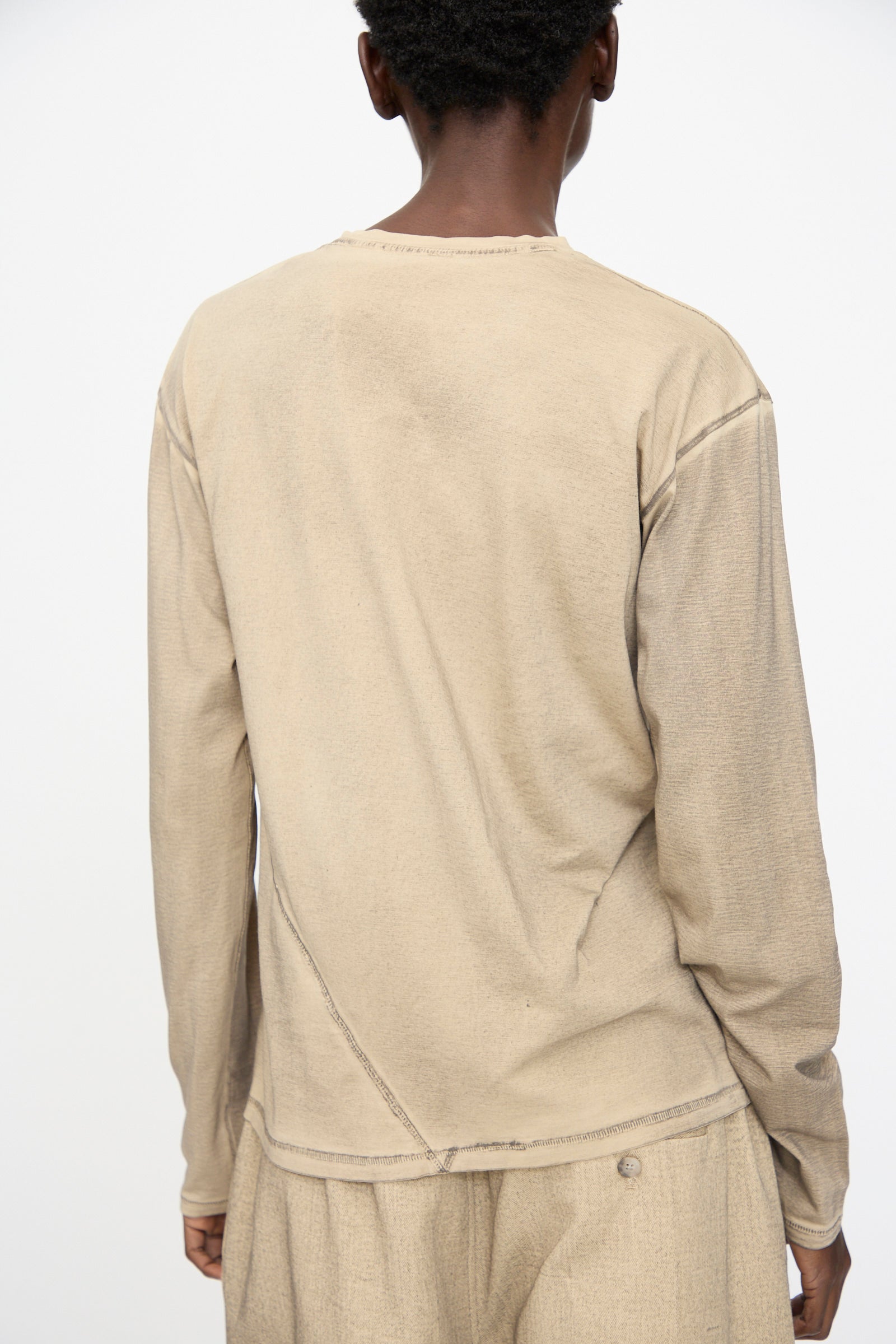 A person stands with their back to the camera, wearing the Lauren Manoogian Bias Long Sleeve Tee in Painted Antique, paired with matching pants against a plain background.