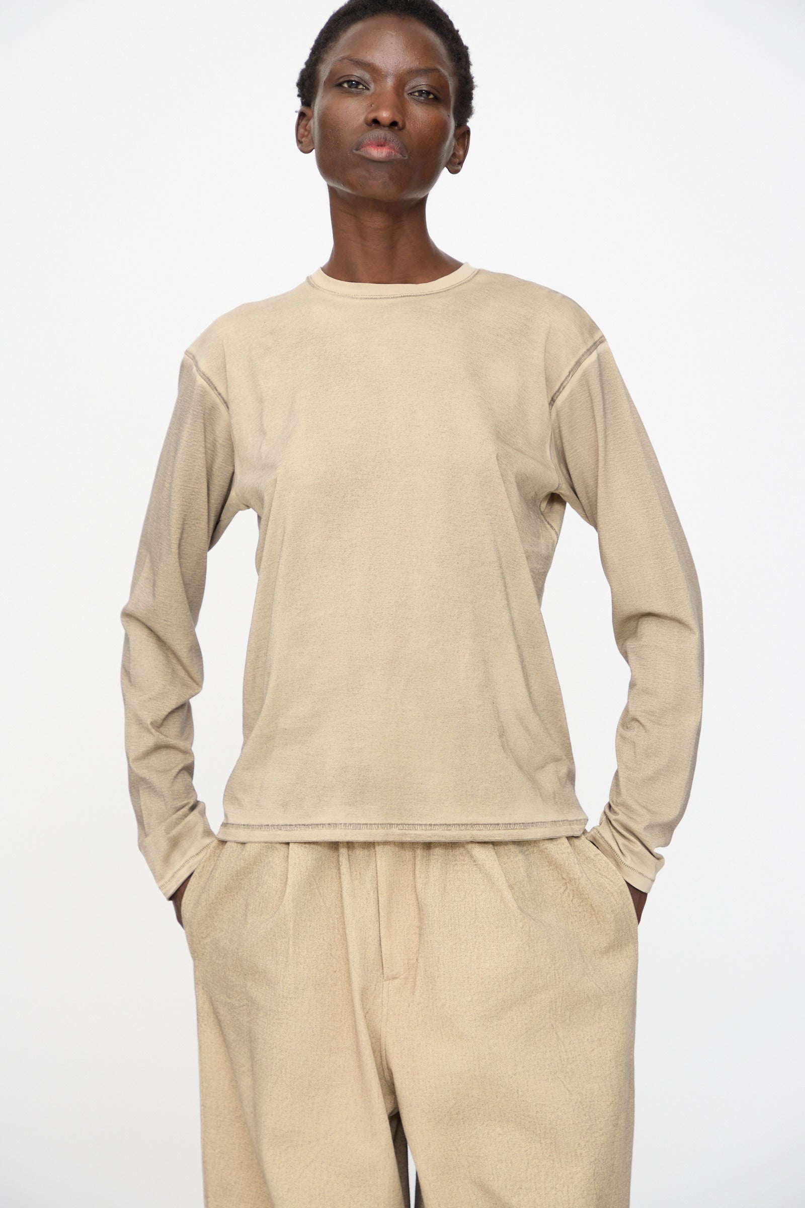 A person wears the Lauren Manoogian Bias Long Sleeve Tee in Painted Antique with matching loose pants, standing against a plain white background and looking directly at the camera.