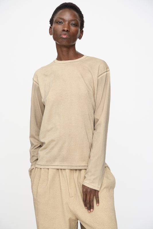 A person wearing the Lauren Manoogian Bias Long Sleeve Tee in Painted Antique and matching beige pants stands against a plain white background.