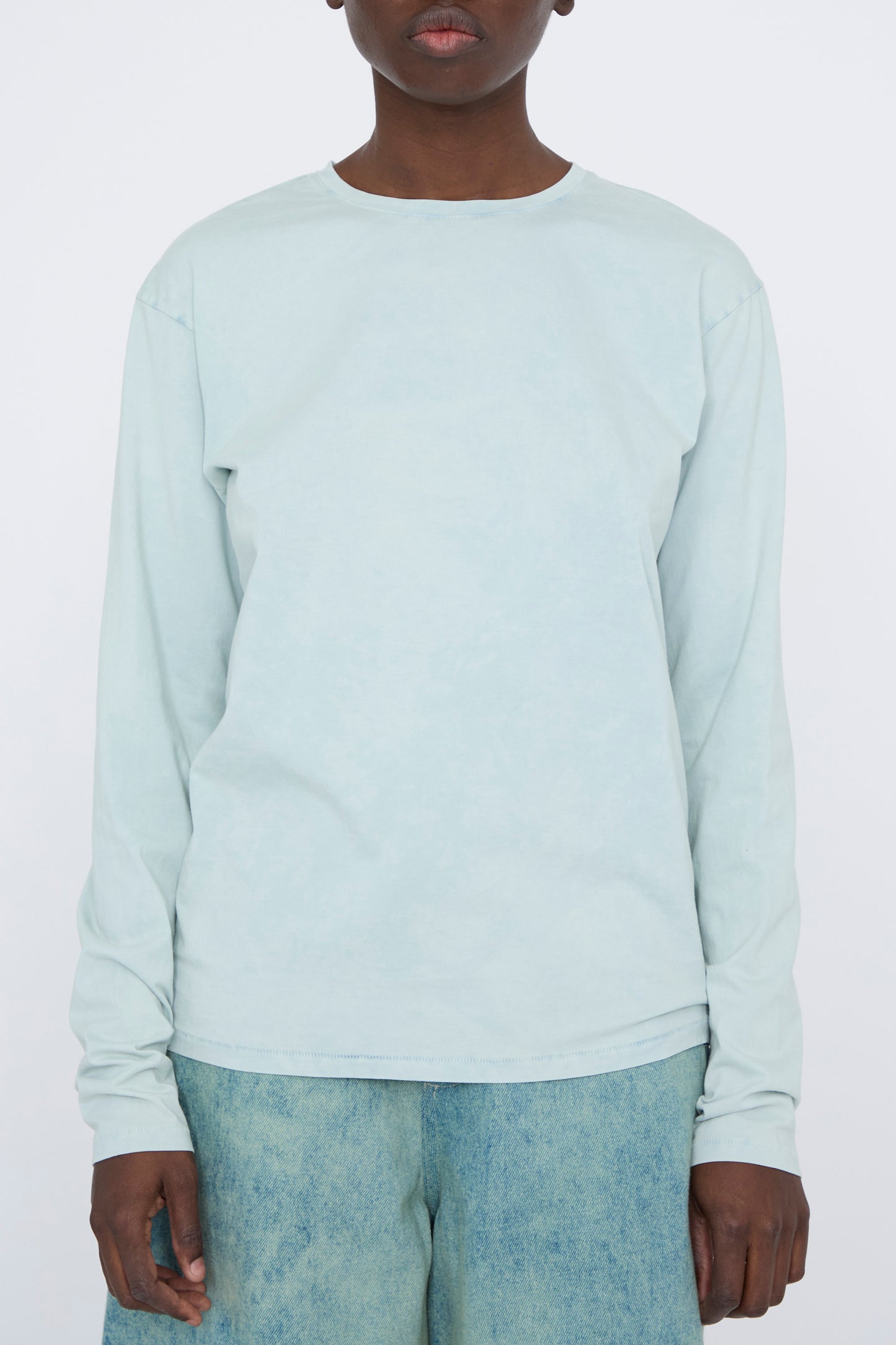 A person wearing a Bias Long Sleeve Tee in Acid by Lauren Manoogian and faded jeans stands against a plain background.