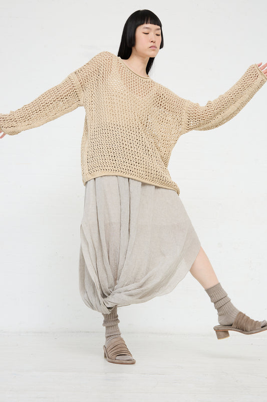 Woman in a beige Lauren Manoogian Big Net Pullover and draped skirt striking a dance-like pose against a white background.