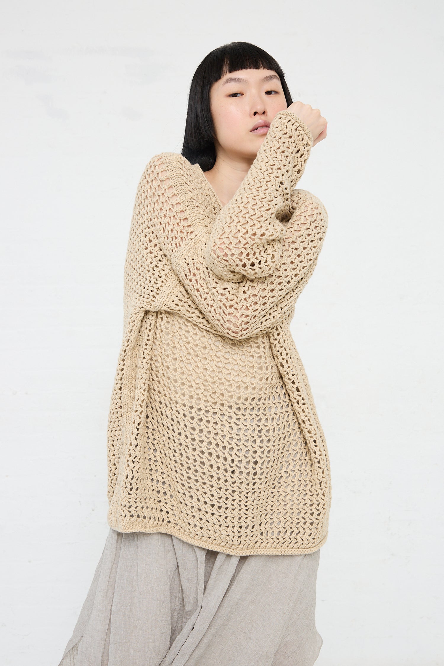 Woman in a Lauren Manoogian Big Net Pullover in Jute posing with one hand near her face.