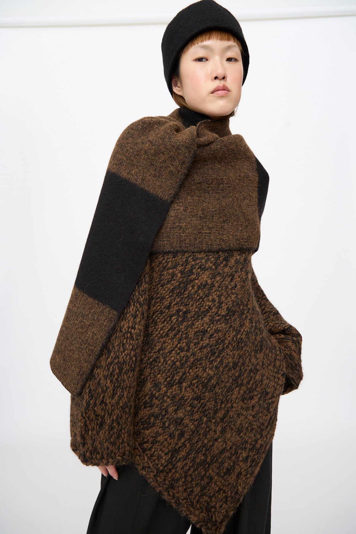 A person wearing a Lauren Manoogian Block Scarf in Rust Marl and Black over a textured brown sweater and a black hat.