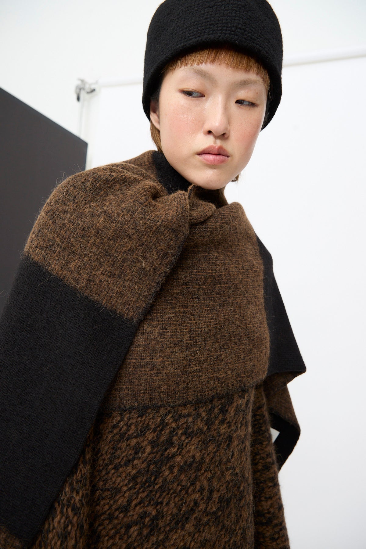 Person wearing a black knit hat and a Lauren Manoogian Block Scarf in Rust Marl and Black.