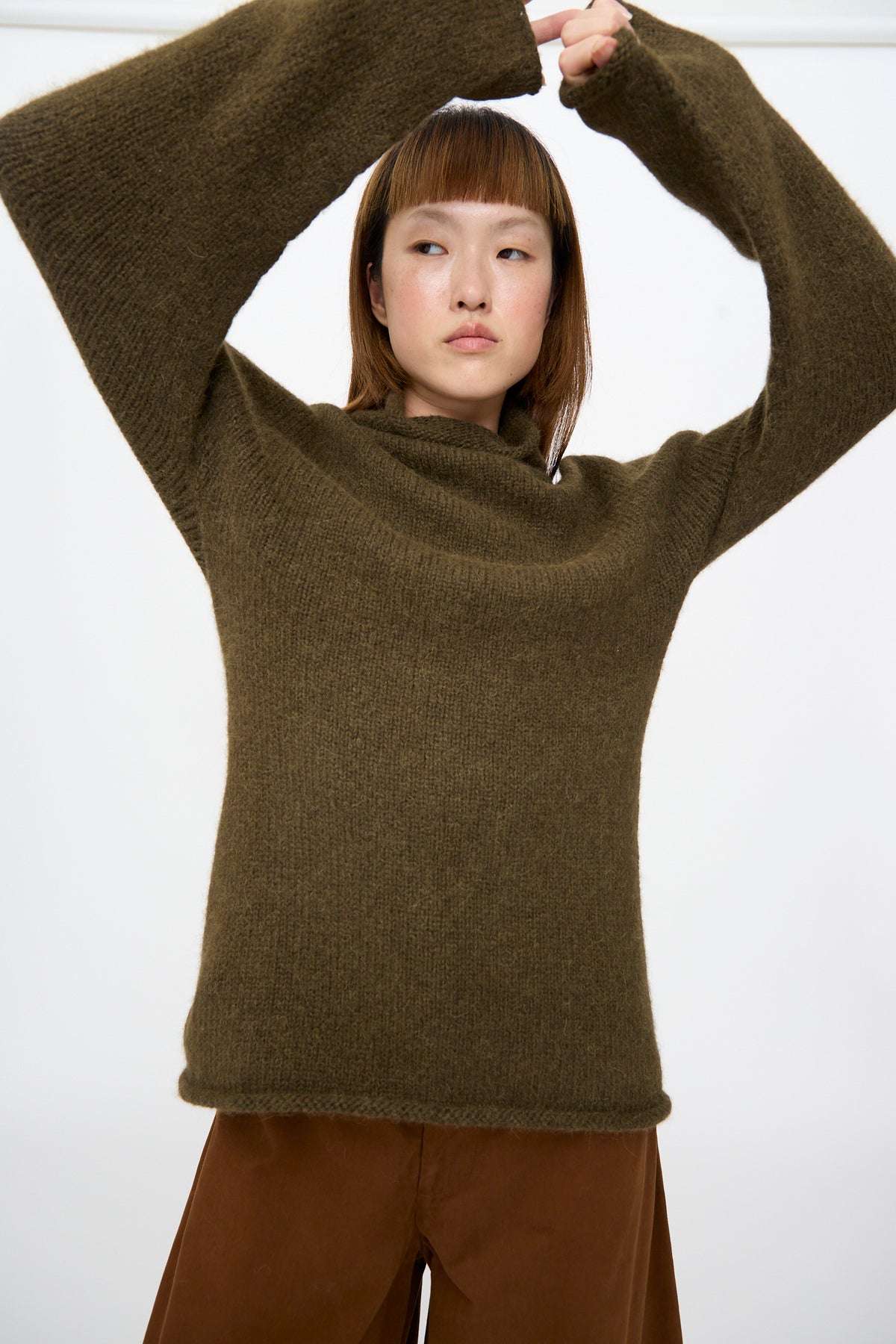 Person wearing a Lauren Manoogian Bottle Turtleneck in Olive with long sleeves raised above their head.