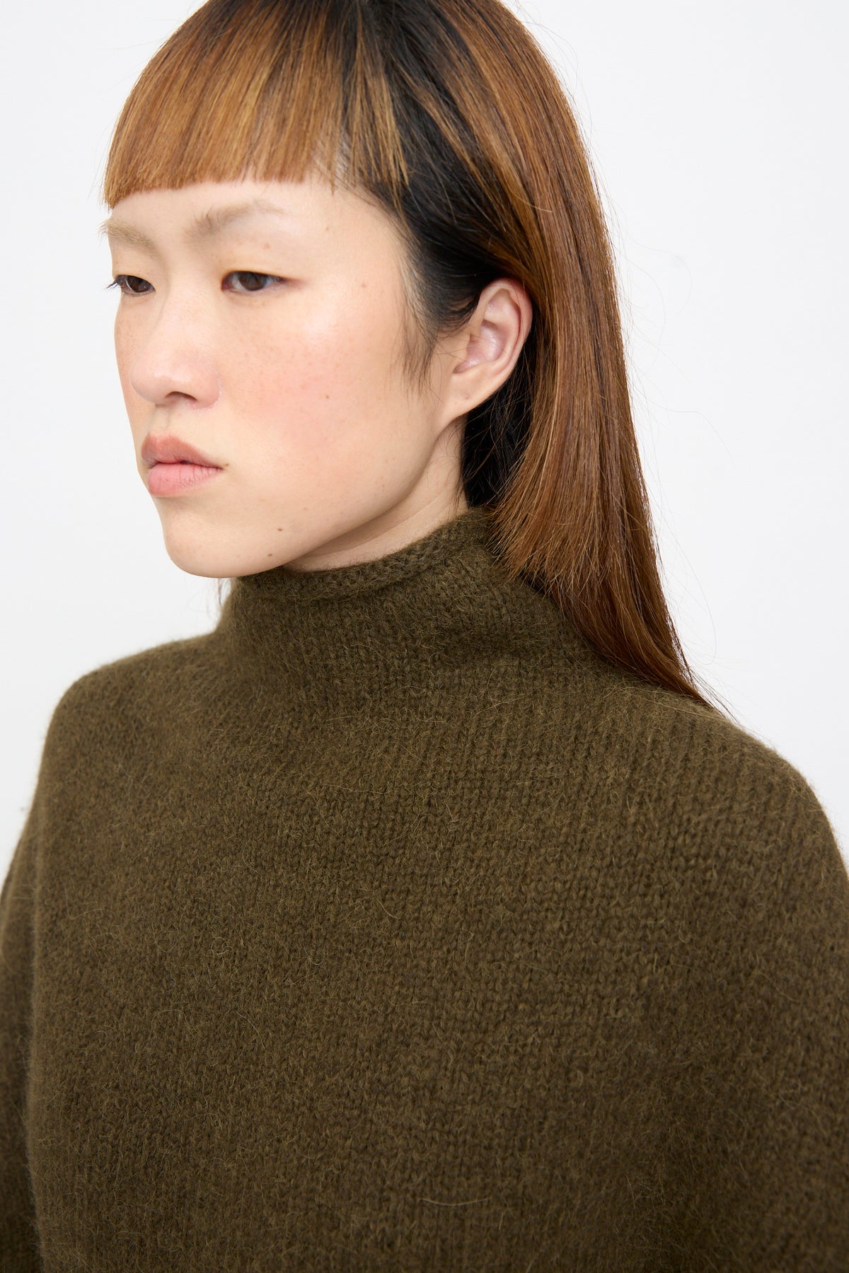 A close up of a person wearing a Lauren Manoogian Bottle Turtleneck in Olive