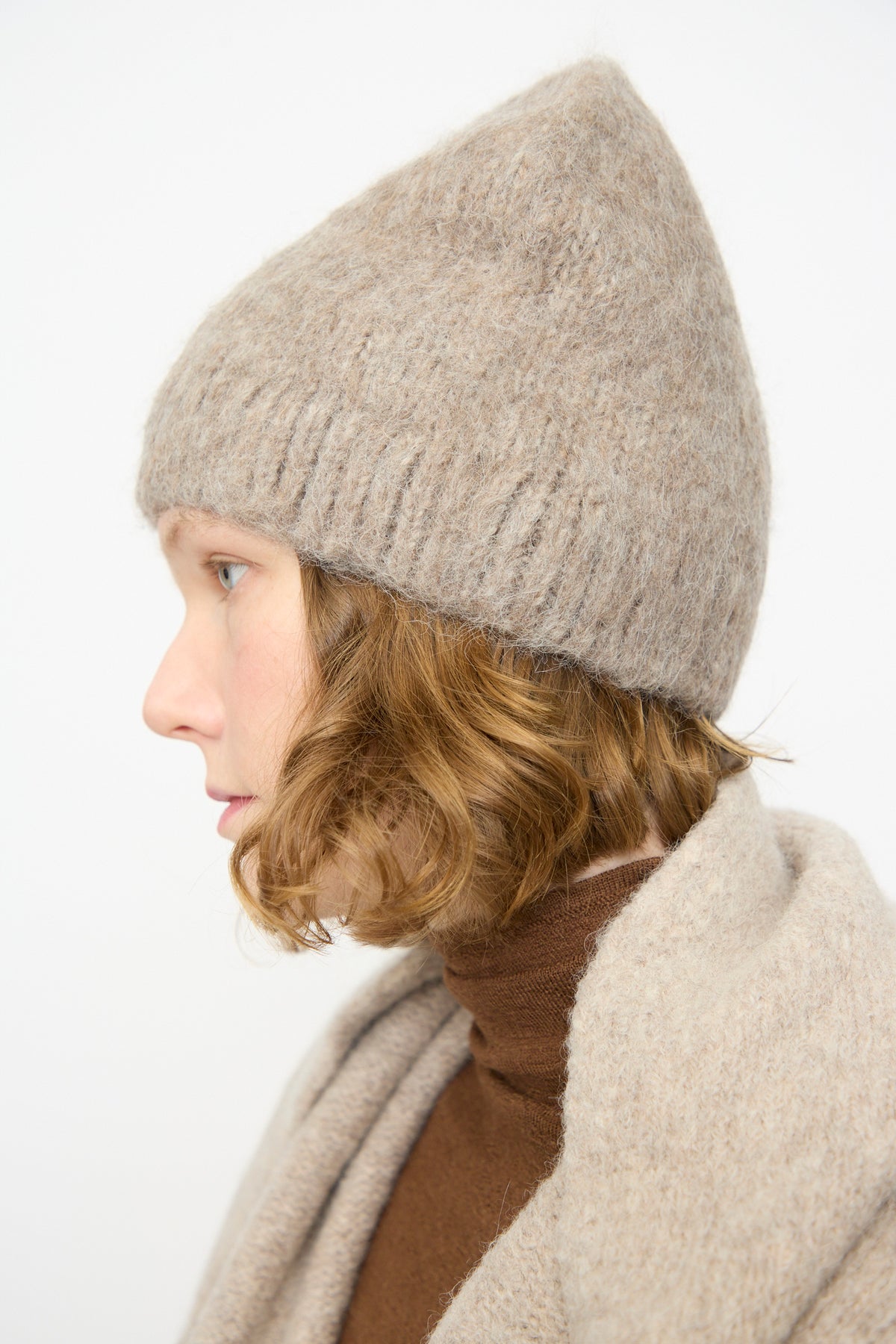 A person in profile view wearing the Lauren Manoogian Brushed Beanie in Grey Melange, a brown turtleneck sweater, and a beige shawl against a plain white background.