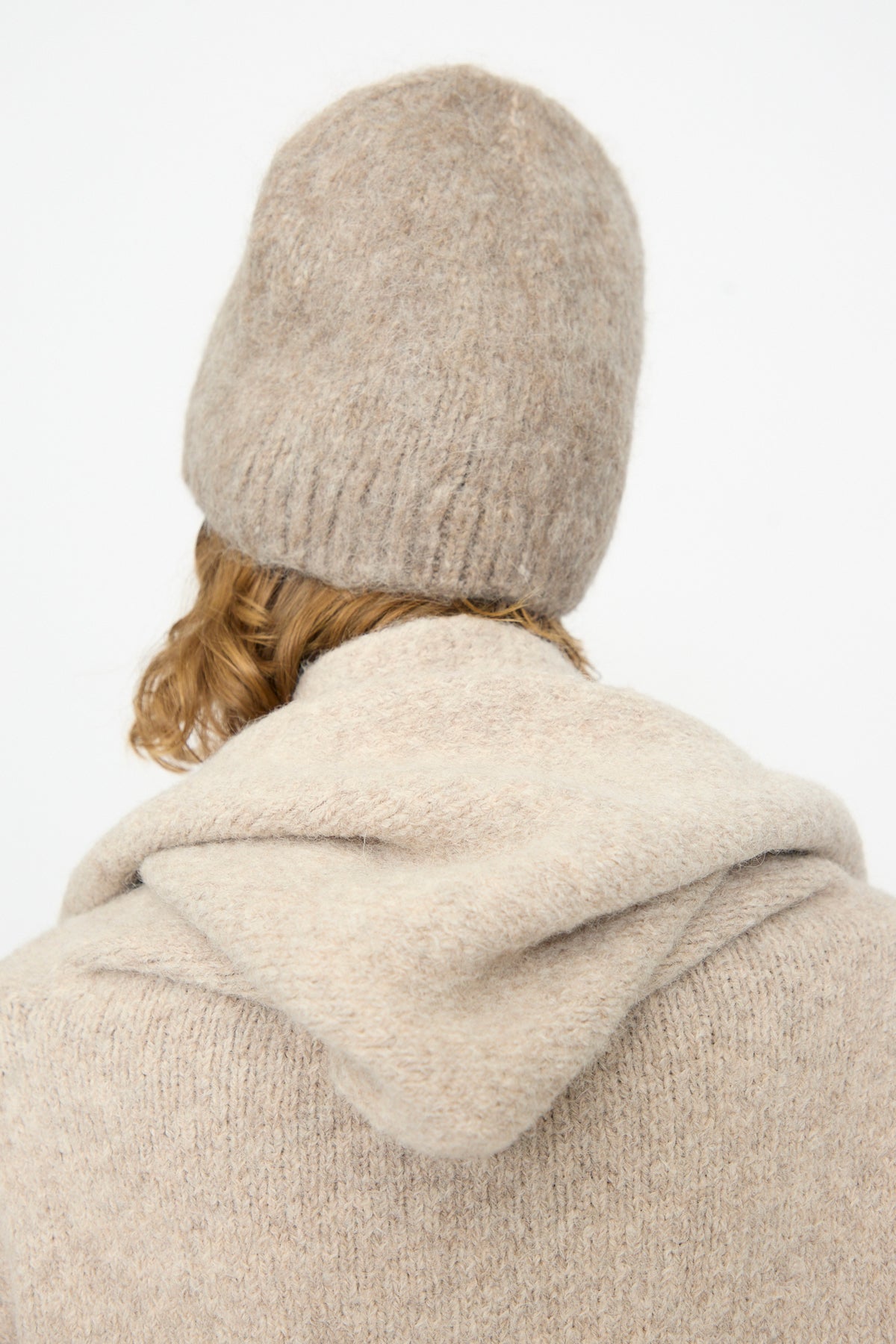 A person with light brown hair is photographed from behind against a plain white background, wearing the Lauren Manoogian Brushed Beanie in Grey Melange and a matching hooded sweater. The cozy alpaca wool hat, handloomed in Peru, adds artisanal charm to the look.
