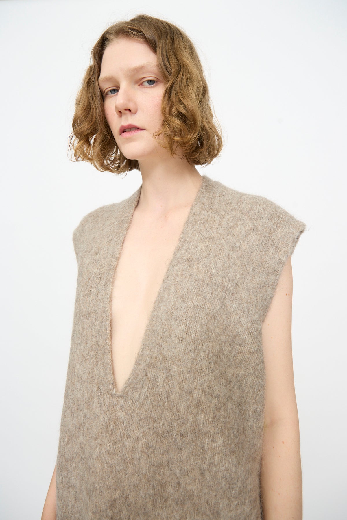 A person with short wavy hair wearing the Lauren Manoogian Brushed Low V Dress in Grey Melange, standing against a plain light background.