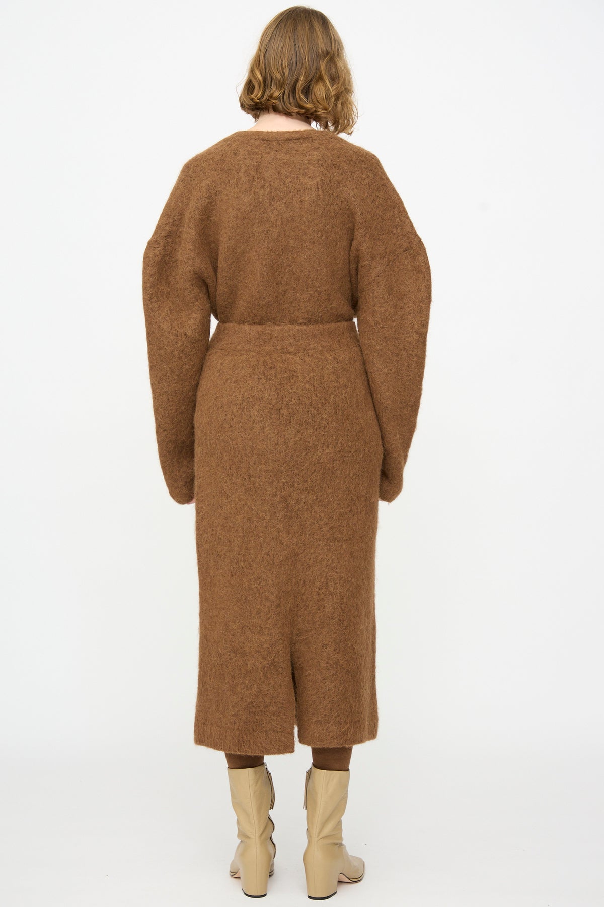 A person with short hair is seen from the back against a plain white background, wearing the Lauren Manoogian Brushed Pencil Skirt in Rust paired with a brown long-sleeve top and beige boots.