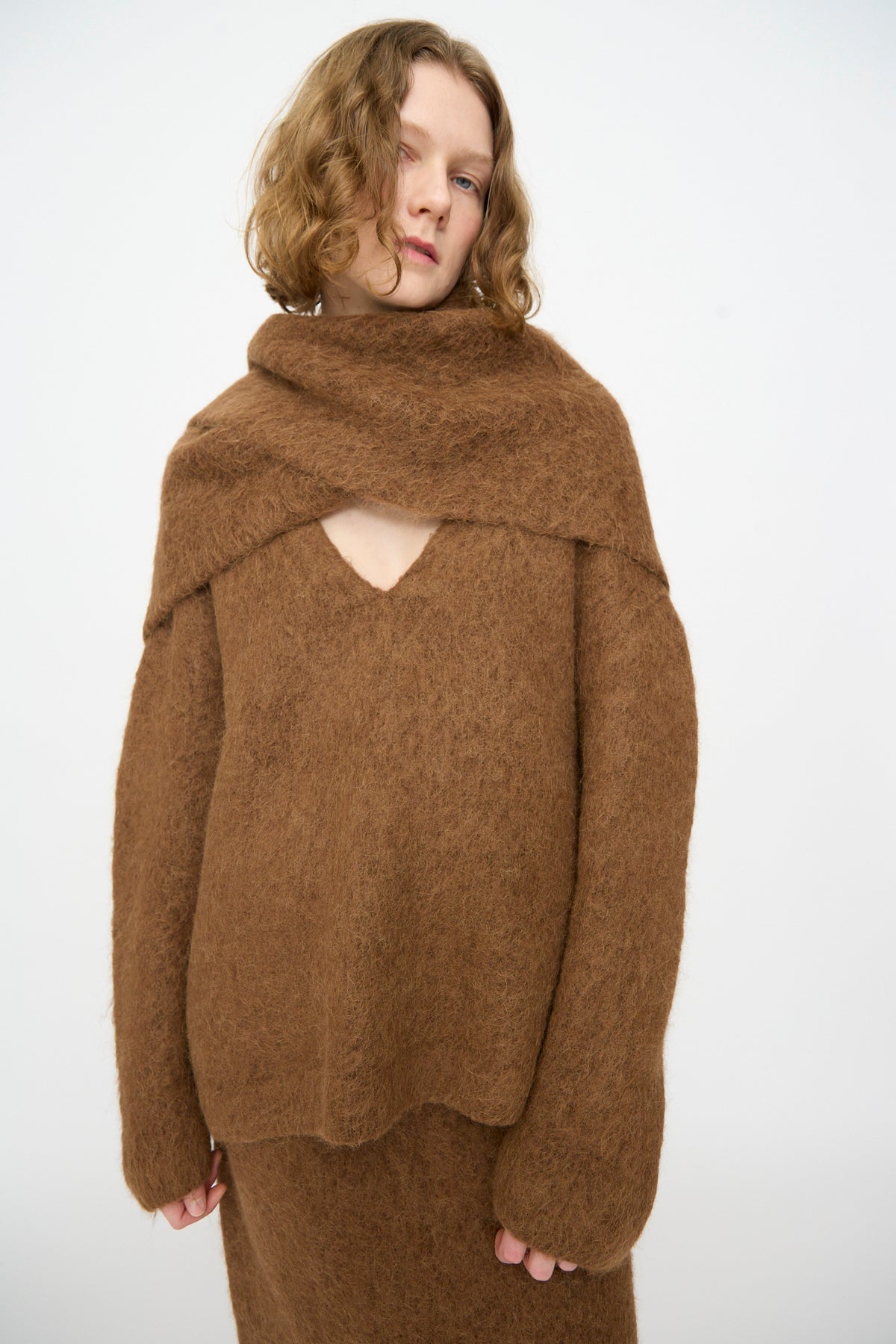 A person wearing a fuzzy brown sweater and the Lauren Manoogian Brushed Triangle Wrap in Rust stands against a plain light background, looking at the camera.