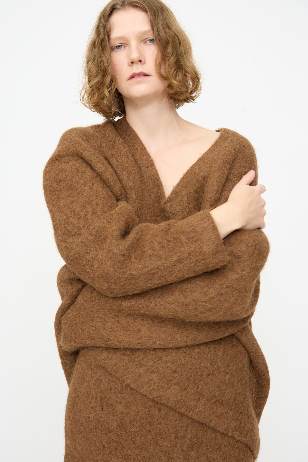 A person with short, wavy blonde hair wears a loose, oversized fit Brushed V Neck in Rust by Lauren Manoogian and a matching skirt, standing against a plain white background with a neutral expression.