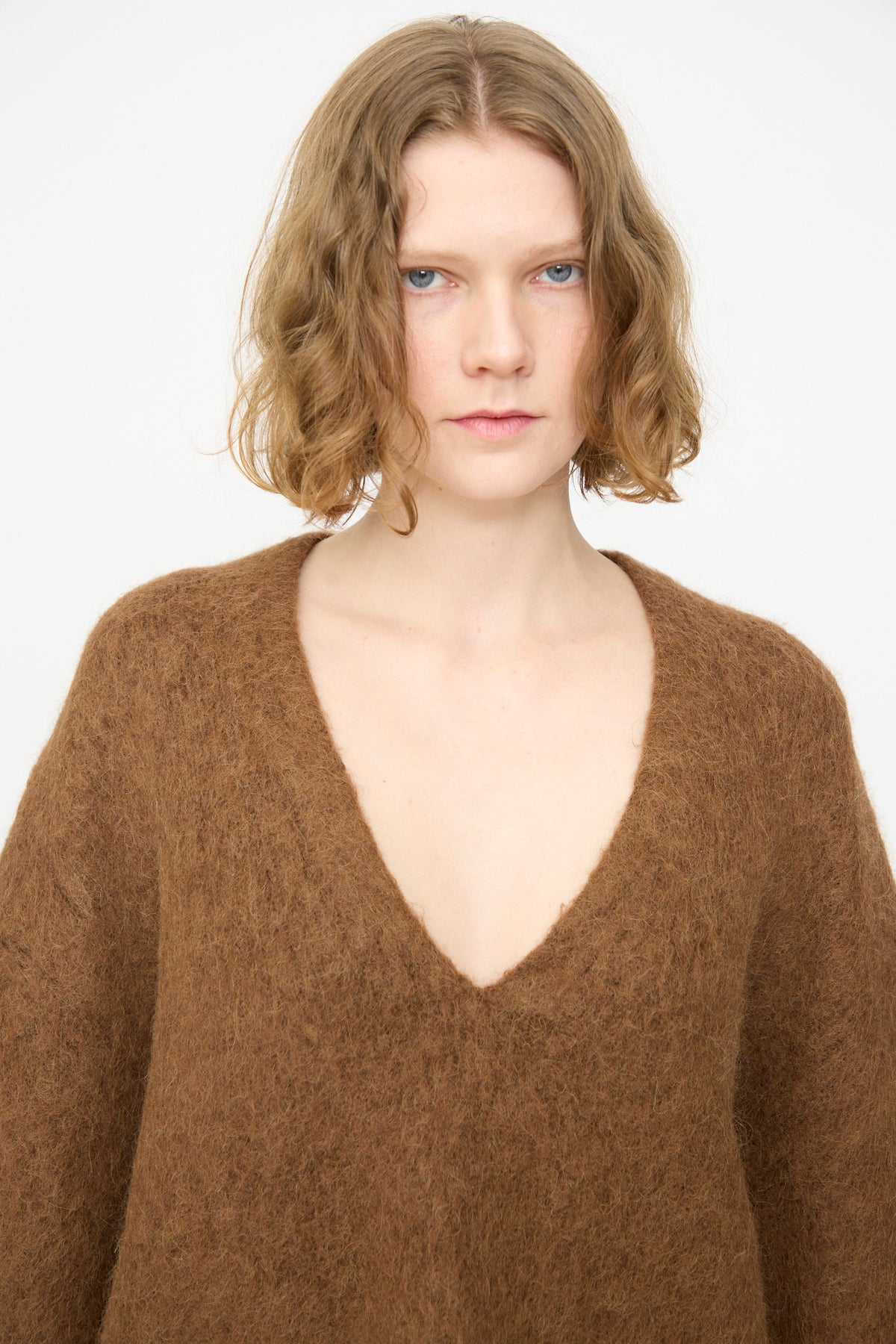 A person with short, wavy light brown hair wears the Lauren Manoogian Brushed V Neck in Rust, featuring an oversized fit, standing against a plain white background.