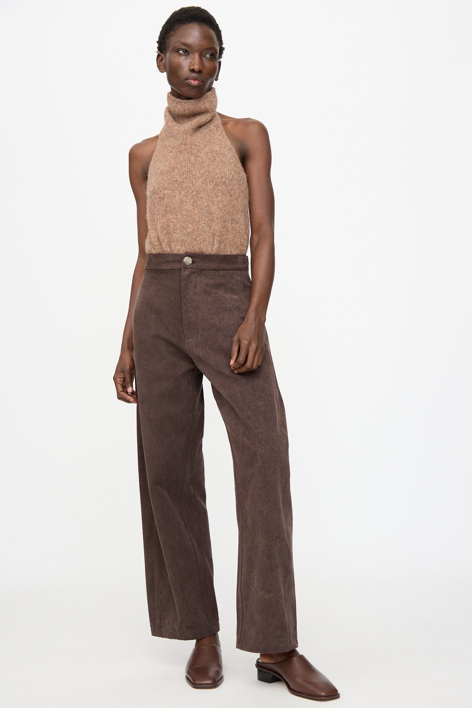 Person wearing a sleeveless brown turtleneck top, Lauren Manoogian Canvas Pants in Washed Soil, and brown slip-on shoes, standing against a white background.