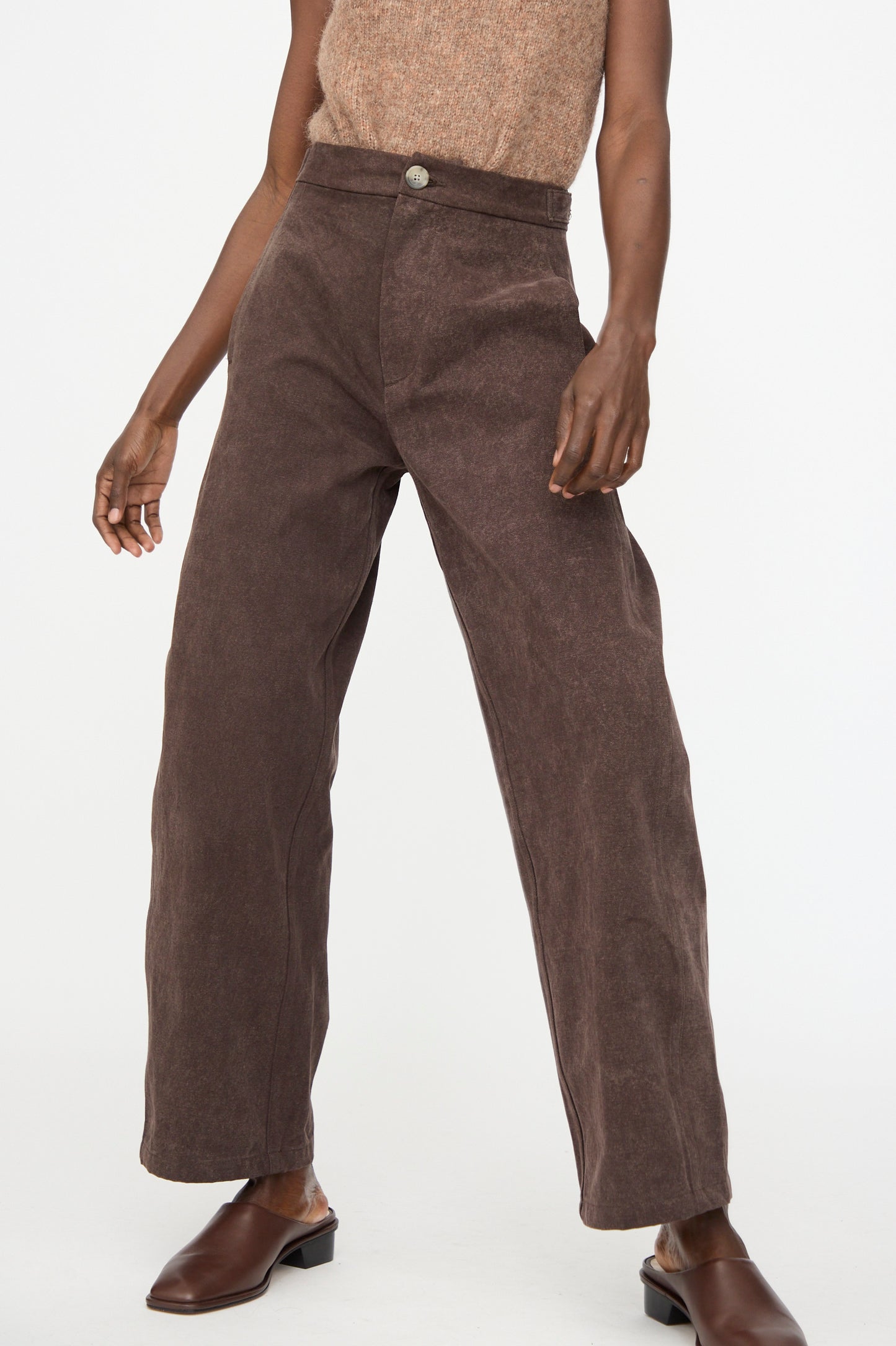 A person wears Lauren Manoogian Canvas Pants in Washed Soil with a sleeveless hand-dyed beige cotton top and brown slip-on shoes, standing against a plain white background.