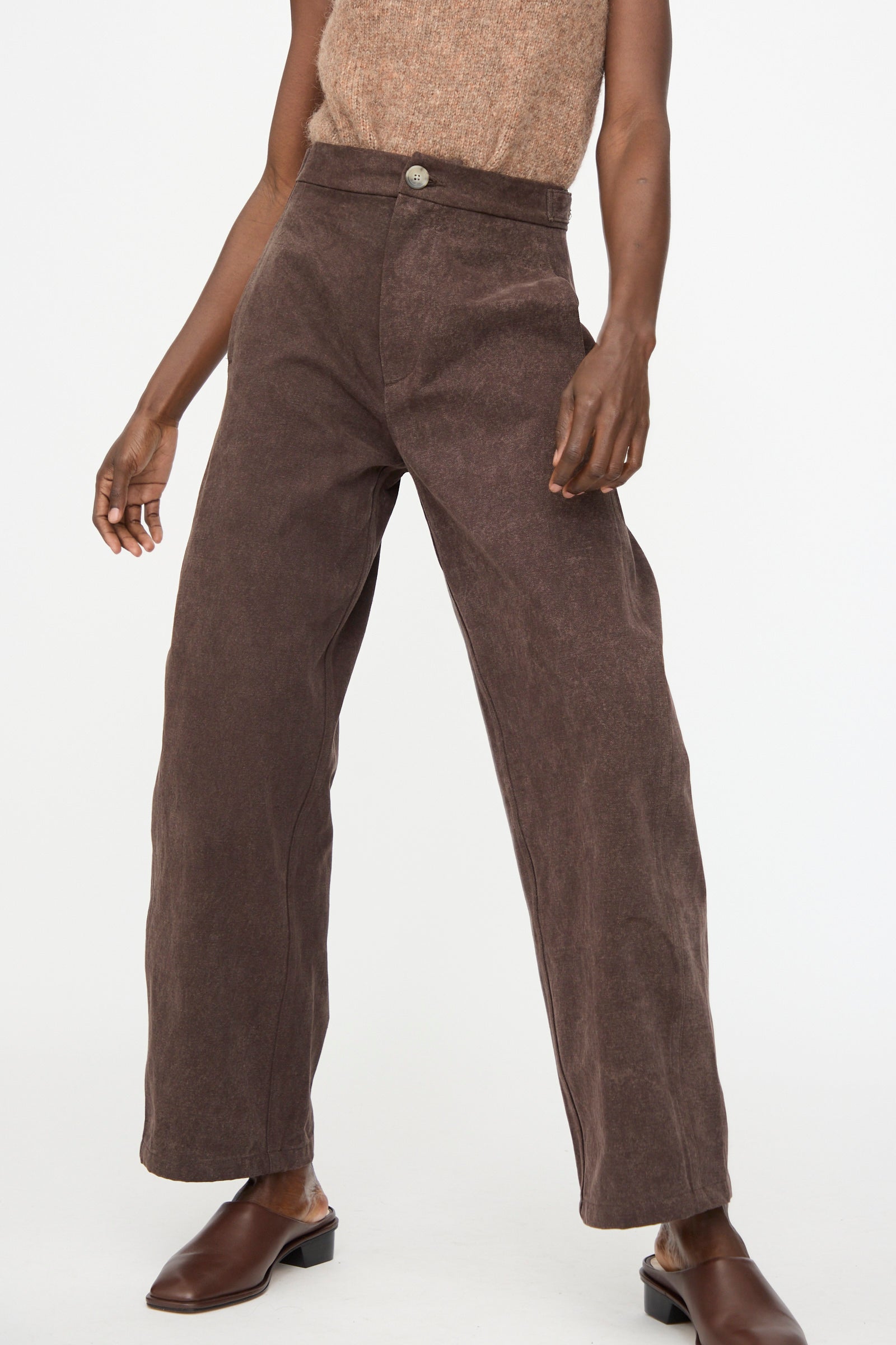 A person wears Lauren Manoogian Canvas Pants in Washed Soil with a sleeveless hand-dyed beige cotton top and brown slip-on shoes, standing against a plain white background.
