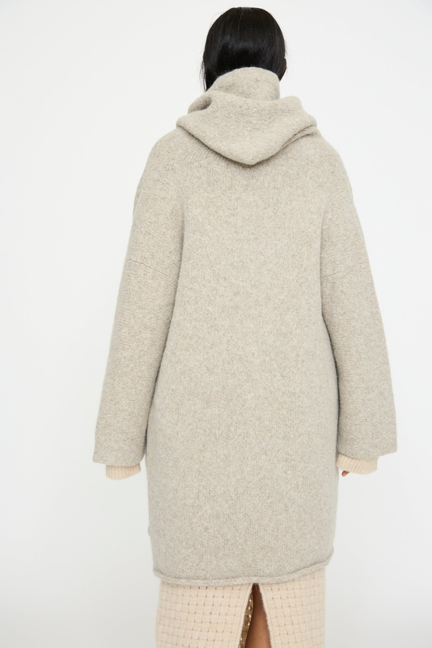 A person wearing a relaxed-fit Lauren Manoogian Capote Coat in Pebble, with a long hood and crafted from alpaca wool, stands with their back to the camera.