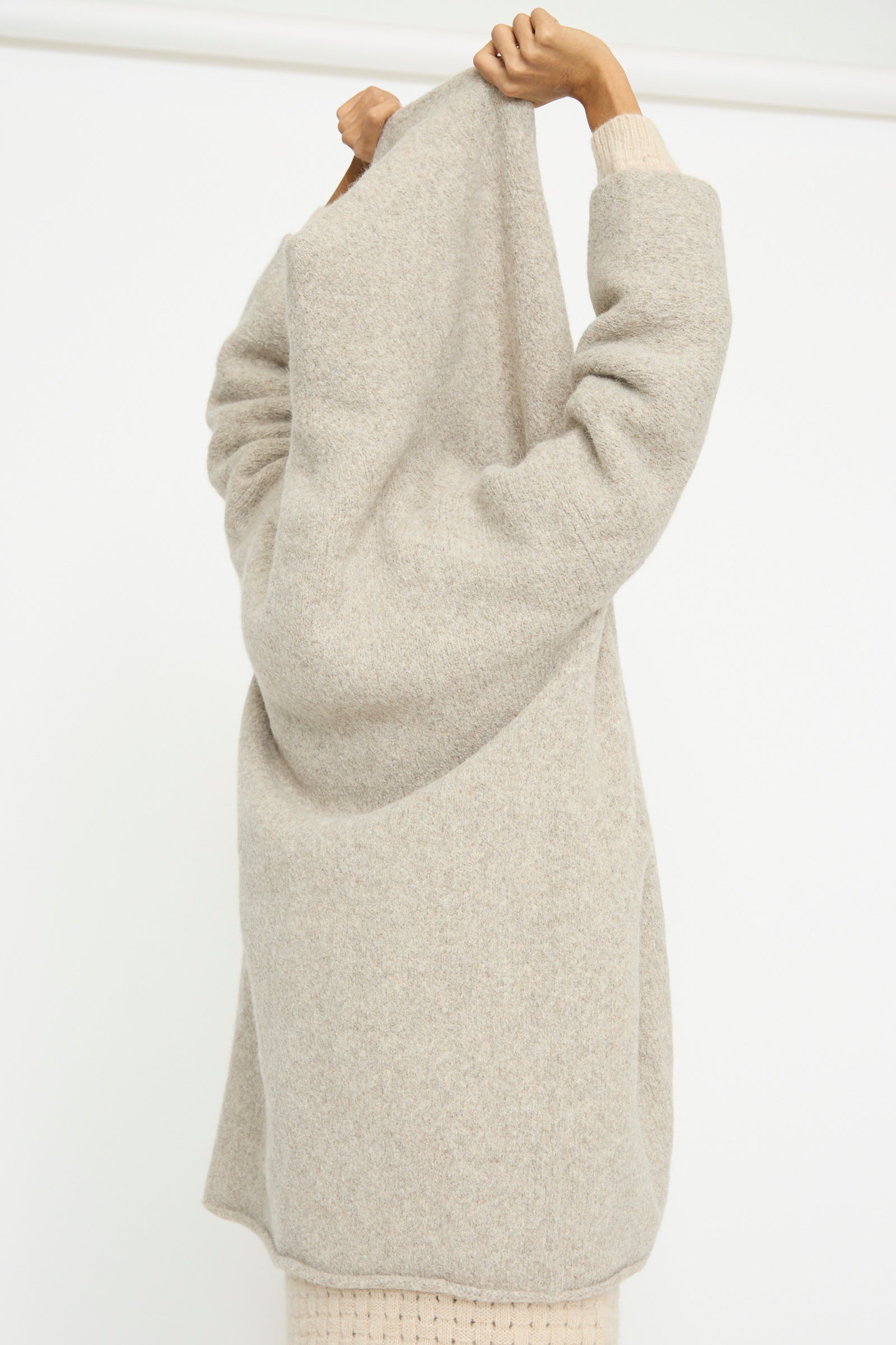 A person faces away in a Lauren Manoogian Capote Coat in Pebble, featuring a relaxed fit with the hood being pulled over their head, stands against a plain white background.