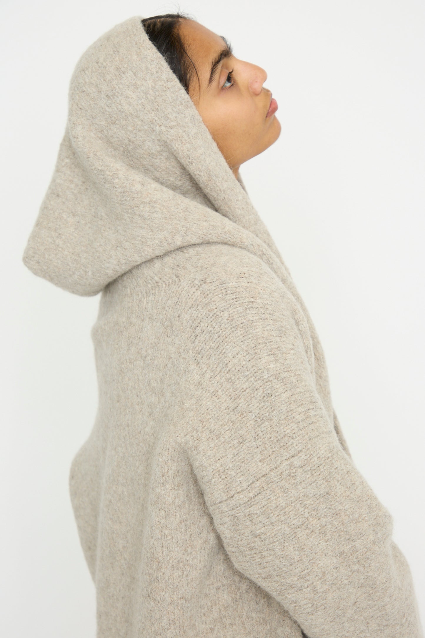 A person in a gray Lauren Manoogian Capote Coat in Pebble gazes upward from the side with their hood on, set against a plain background.