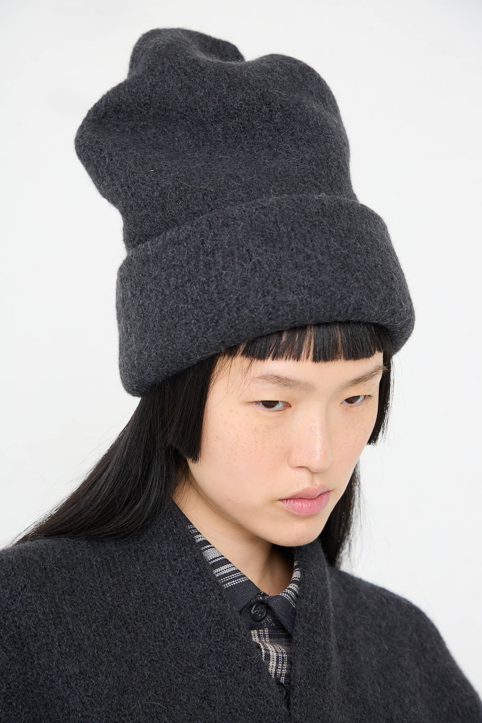 A person with long black hair wears a tall, dark gray Carpenter Hat in Ink by Lauren Manoogian and a matching handloomed sweater, both made in Peru.