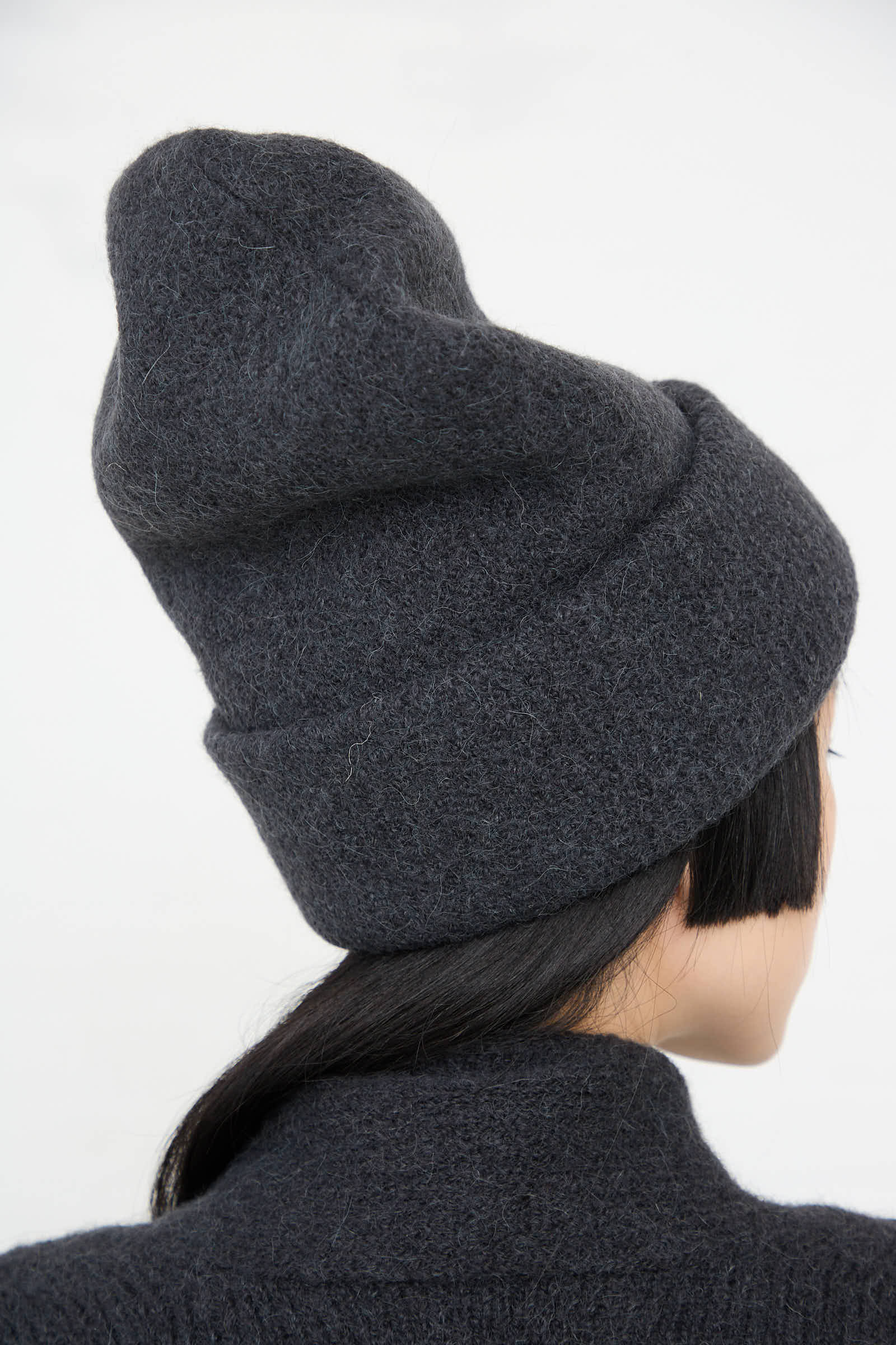 A person with short black hair is shown from behind, wearing a dark gray, handloomed Carpenter Hat in Ink by Lauren Manoogian.