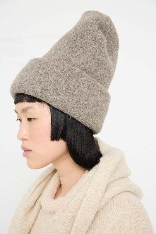 Person in a beige sweater and the Lauren Manoogian Carpenter Hat in Rock. Profile view against a plain white background.