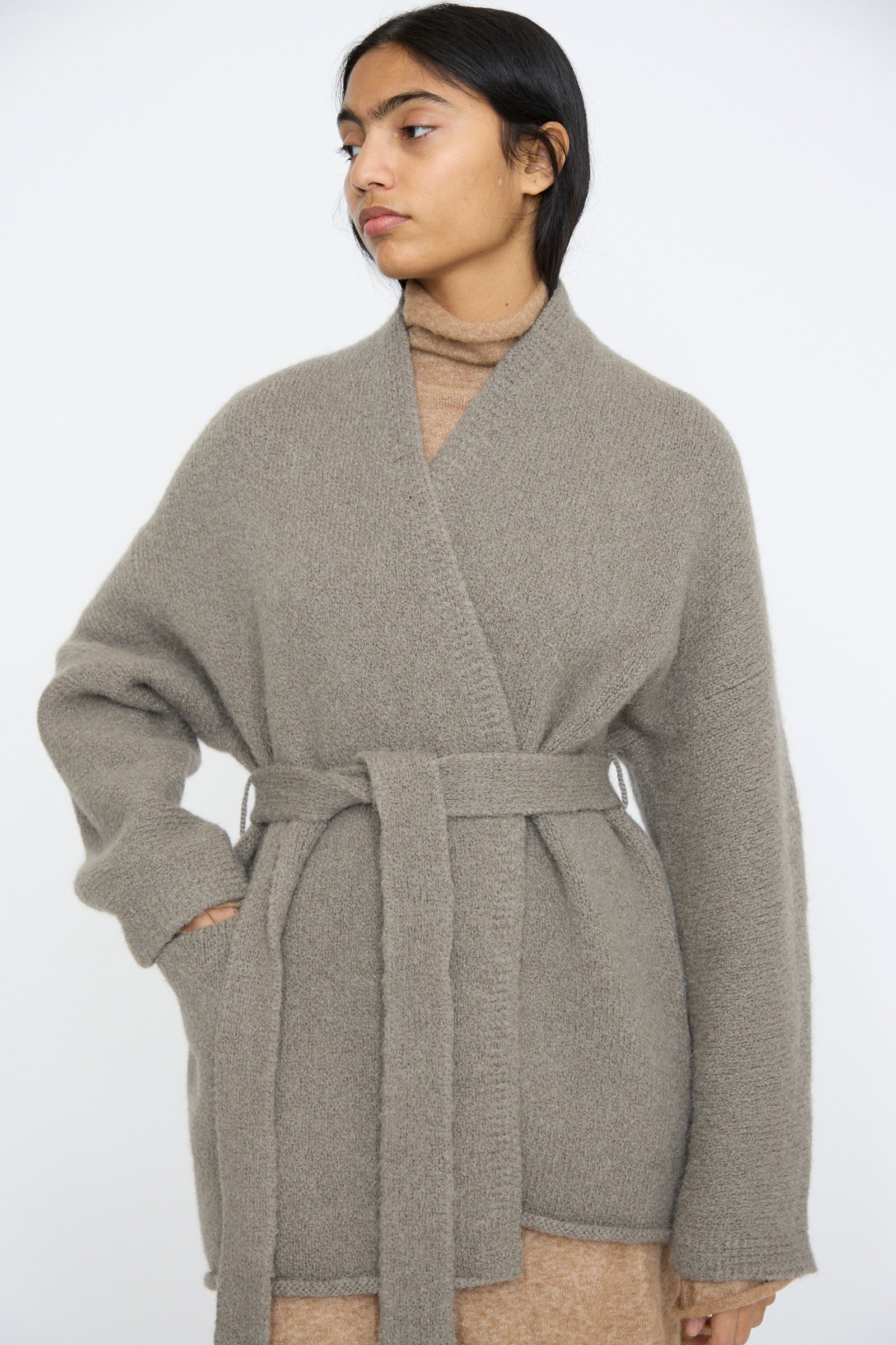 A person models the Lauren Manoogian Coto Cardigan in Concrete and a brown turtleneck against a plain white background.