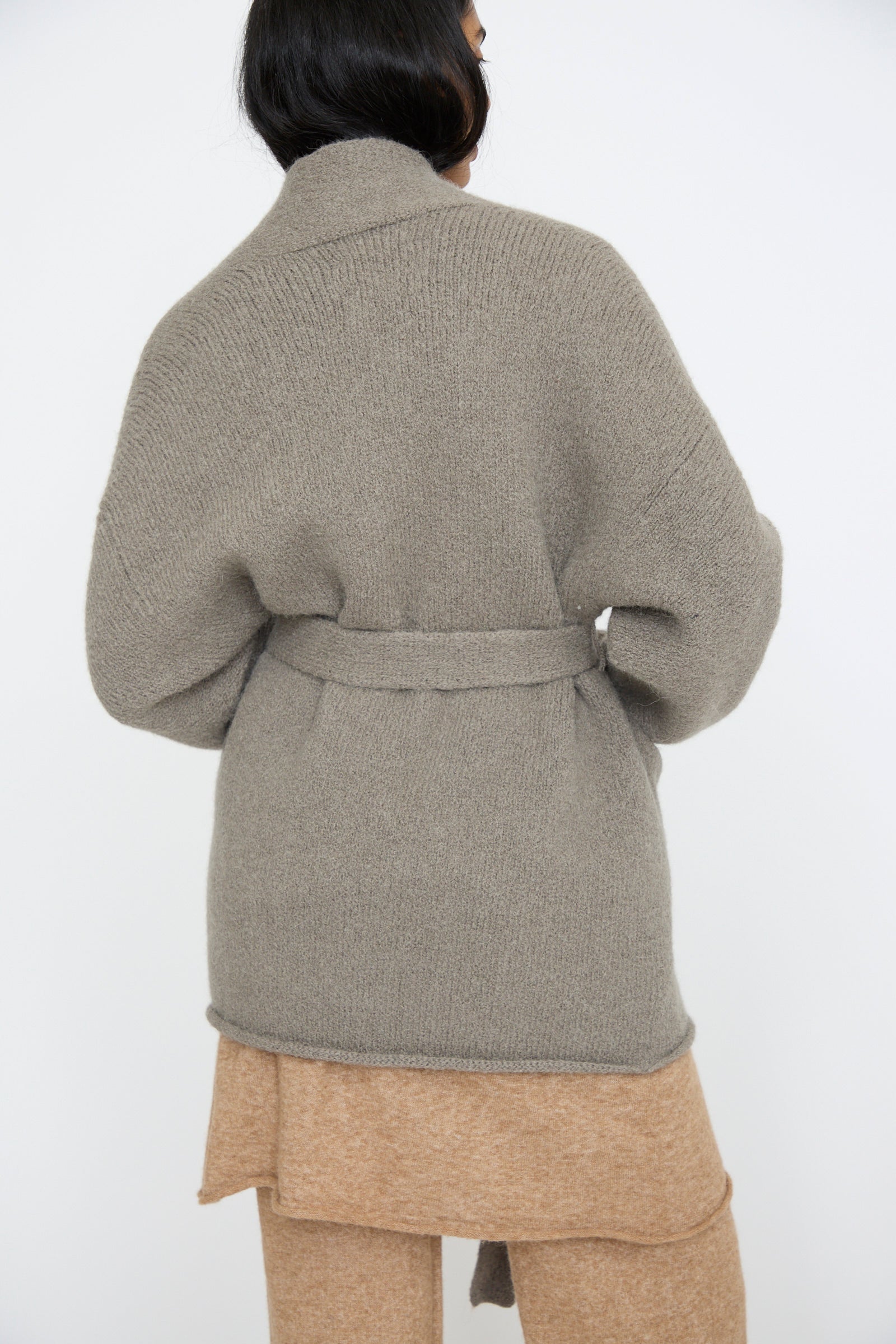 A person faces away wearing a Coto Cardigan in Concrete by Lauren Manoogian, hand-loomed from soft alpaca wool, paired with a beige layered outfit.