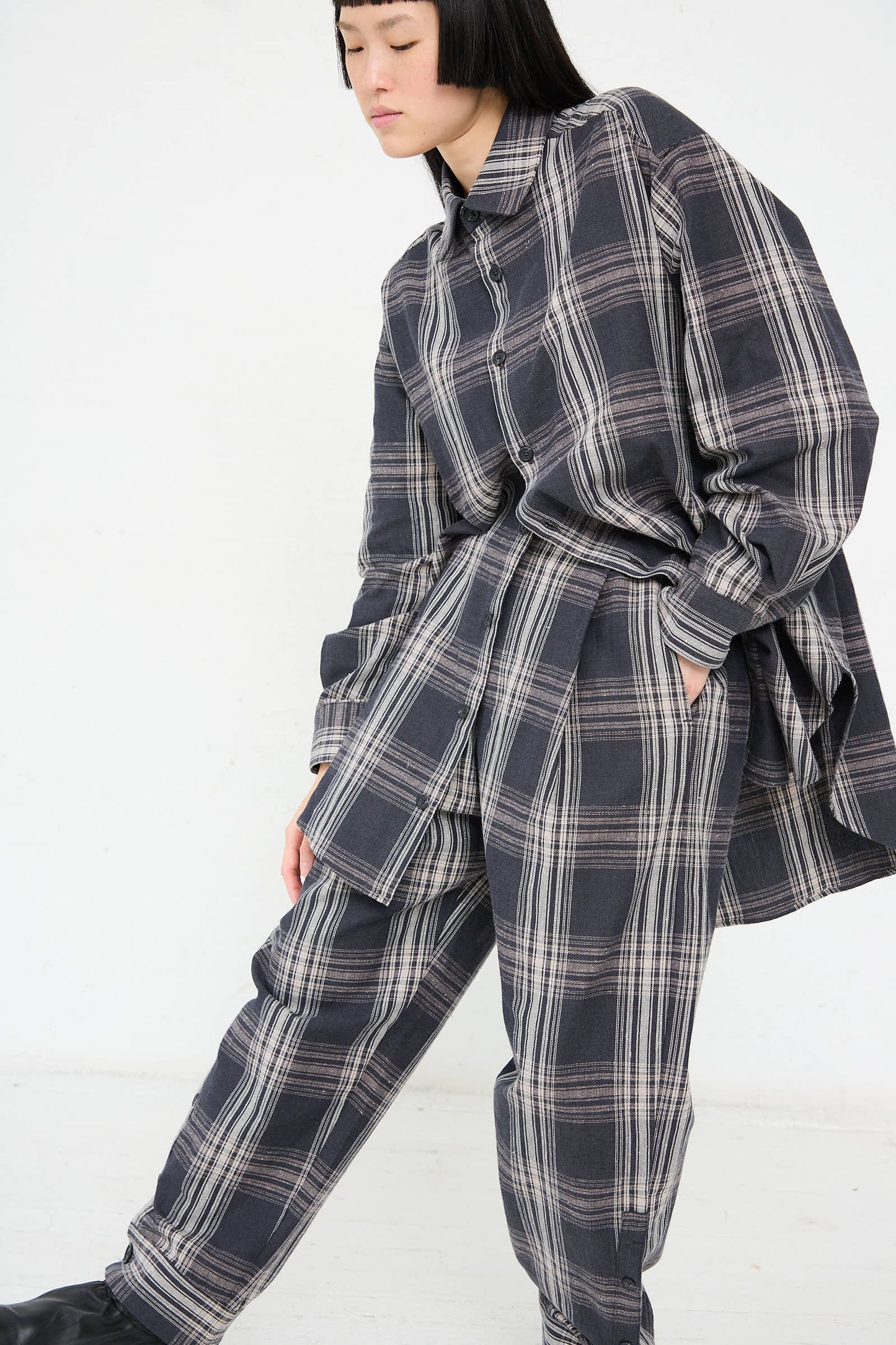 A person wearing the Lauren Manoogian Cotton Cuff Pant in Plaid along with a loose-fitting, dark cotton plaid shirt poses against a plain background.