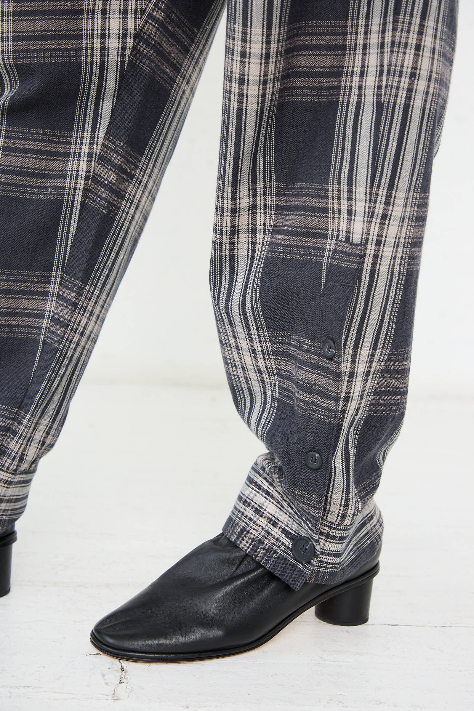 The Lauren Manoogian Cotton Cuff Pant in Plaid, featuring buttoned cuffs and a tapered leg, is worn over black leather shoes with heels.