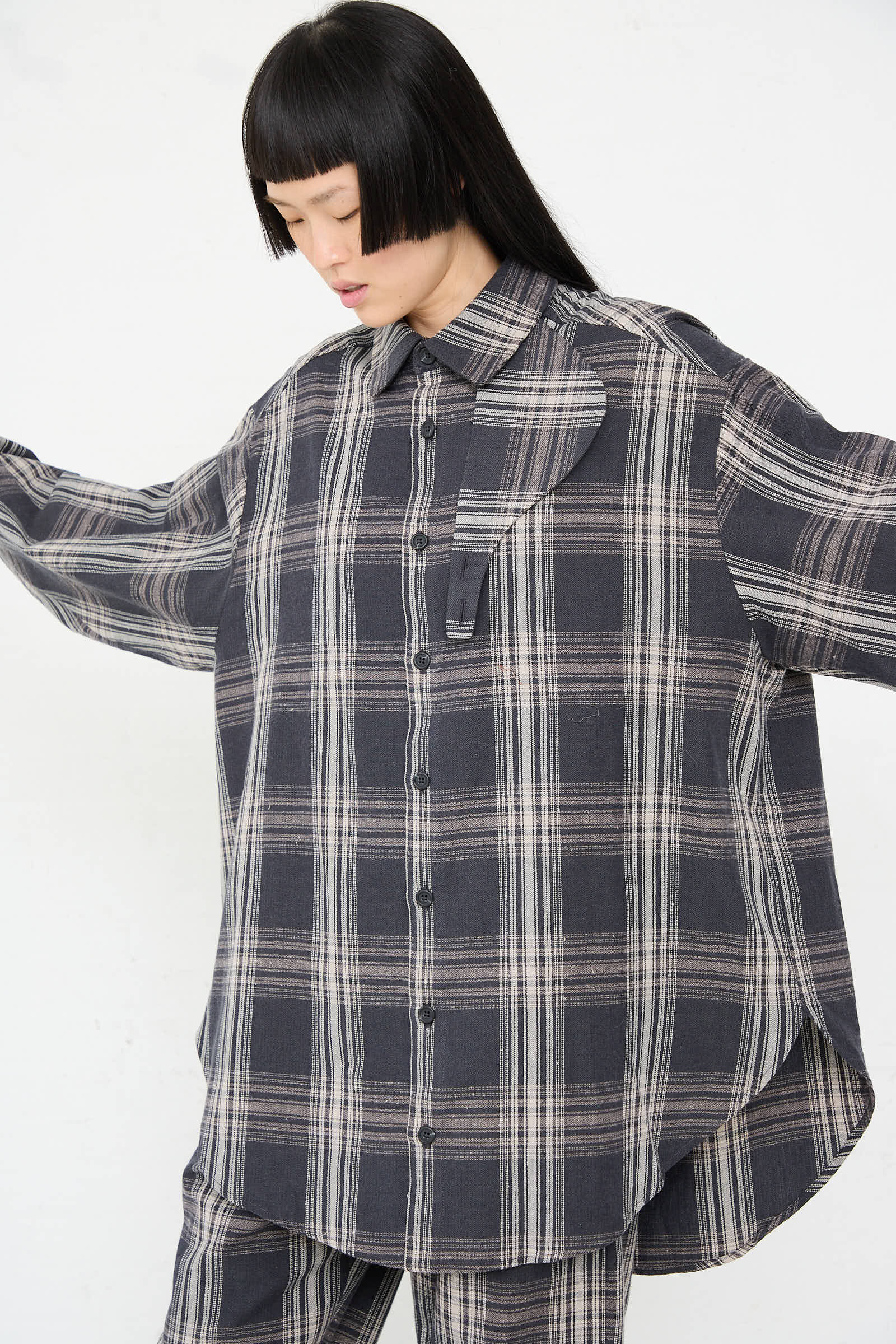 A person with straight black hair is wearing a loose-fitting, oversized Lauren Manoogian Cotton Gaiter Shirt in Plaid and matching cotton pants. Their arms are slightly extended to the sides against a plain background.