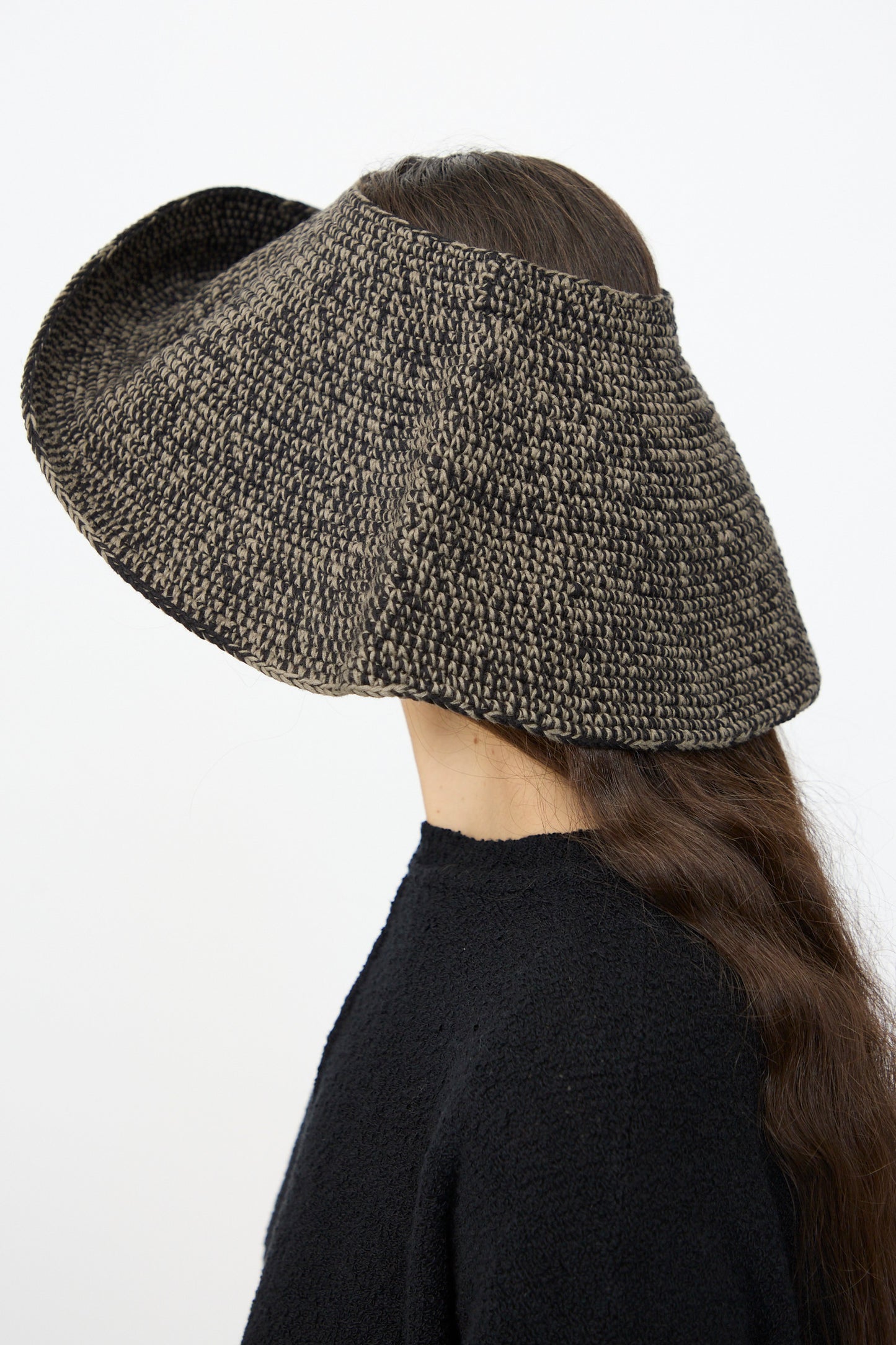 A person with long brown hair wears the Lauren Manoogian Crochet Big Brim Hat in Black Marl, paired with a black marl top, shown in profile against a plain background.