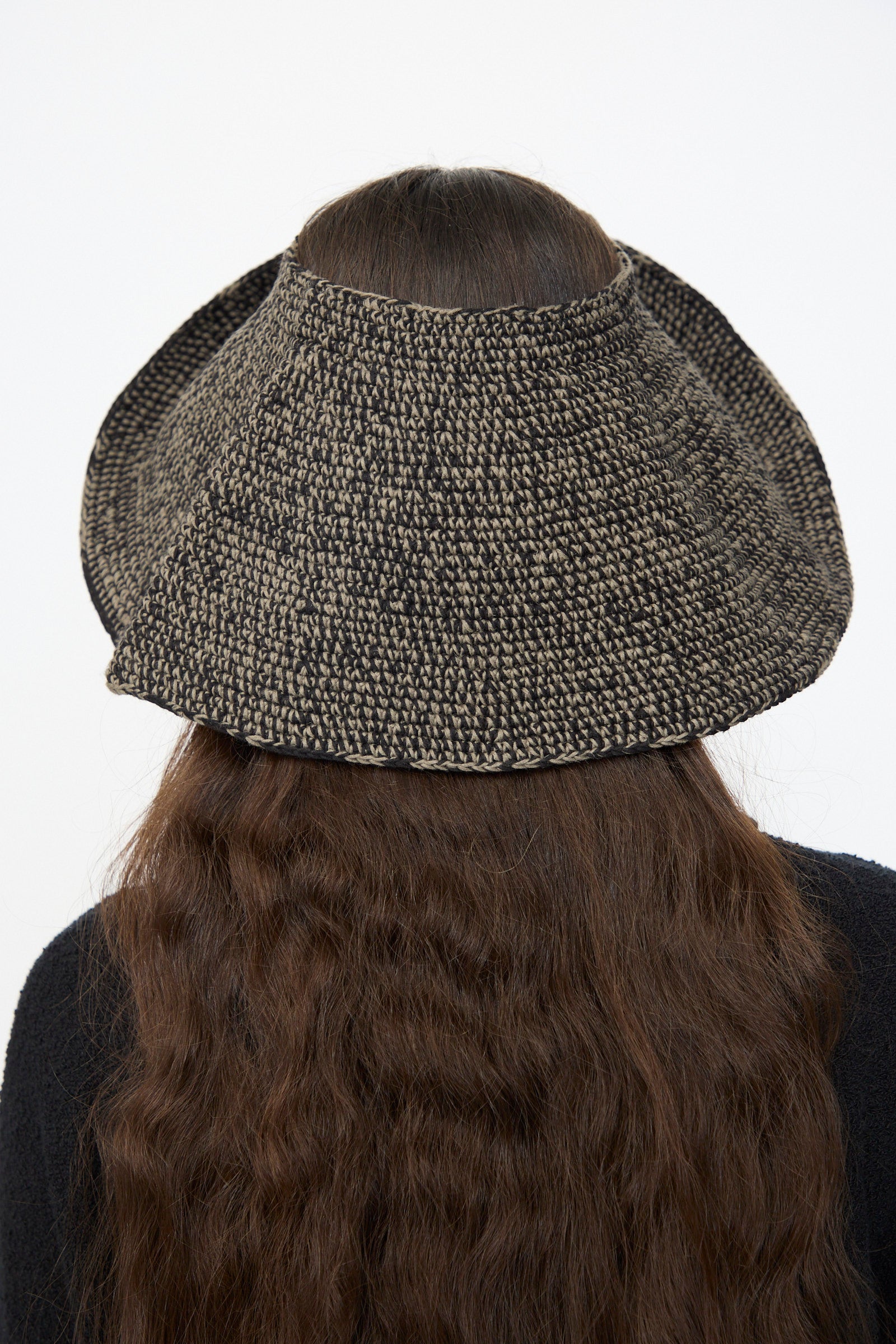 Person with long, wavy brown hair wears the Lauren Manoogian Crochet Big Brim Hat in Black Marl, viewed from the back against a plain background.