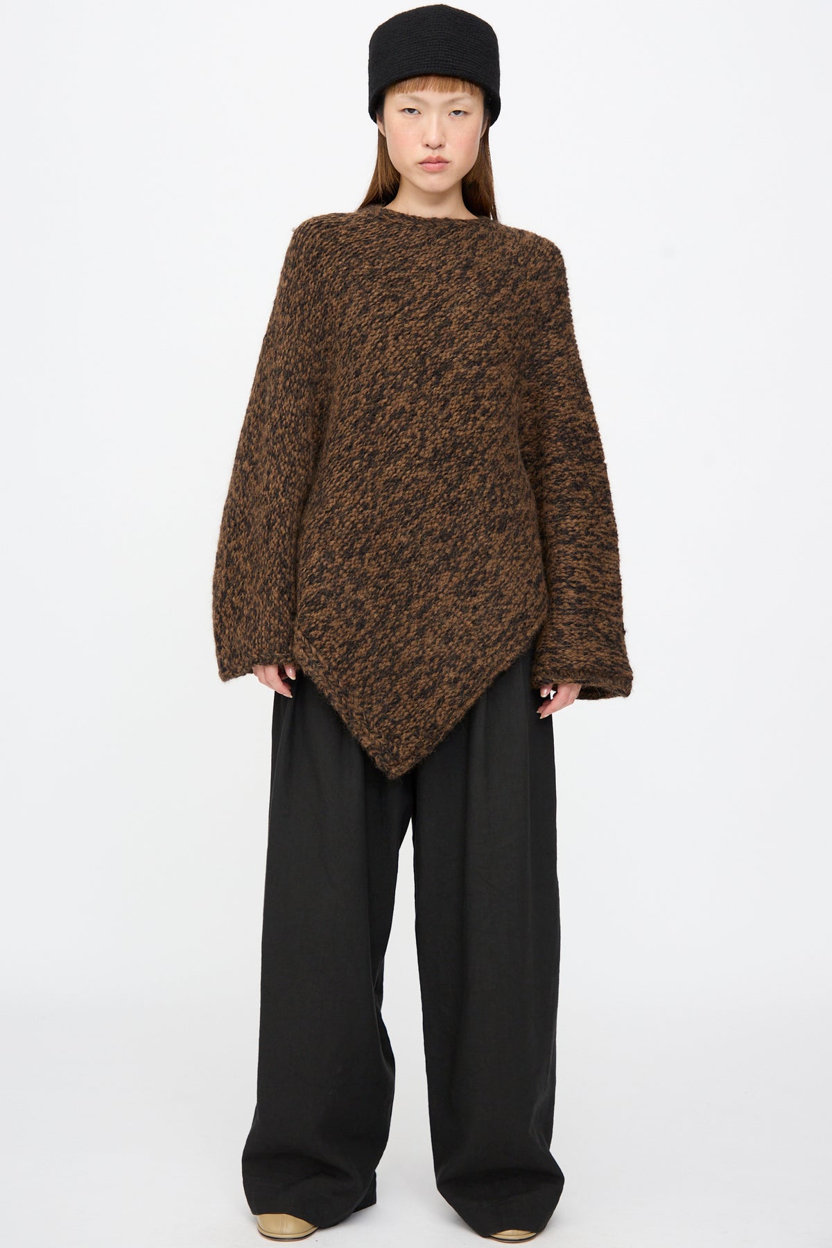 A person wearing a black Lauren Manoogian Crochet Toque, a brown textured asymmetric sweater, and wide-leg black trousers.